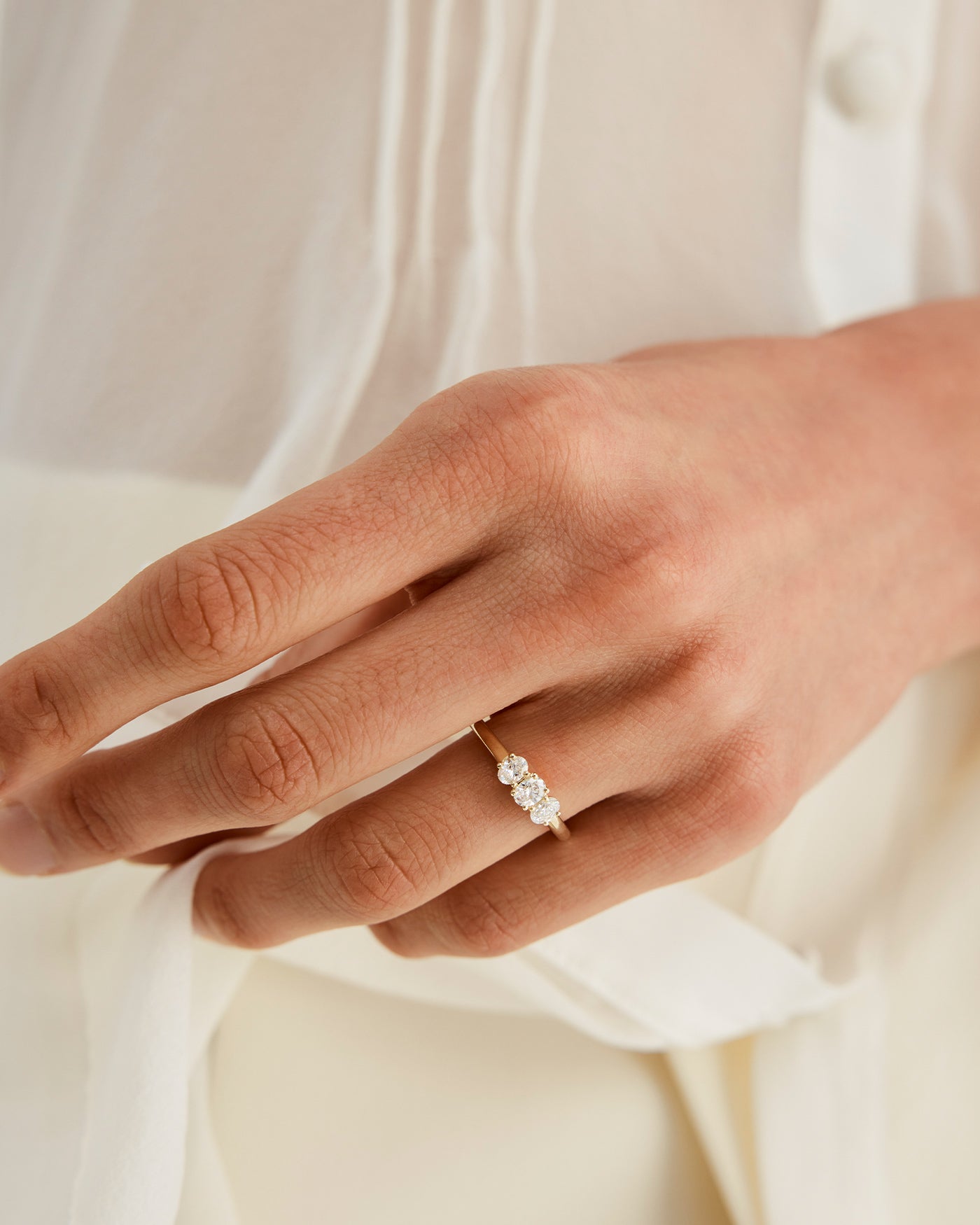 Woman wearing a yellow gold engagement ring with three oval white laboratory grown diamonds.