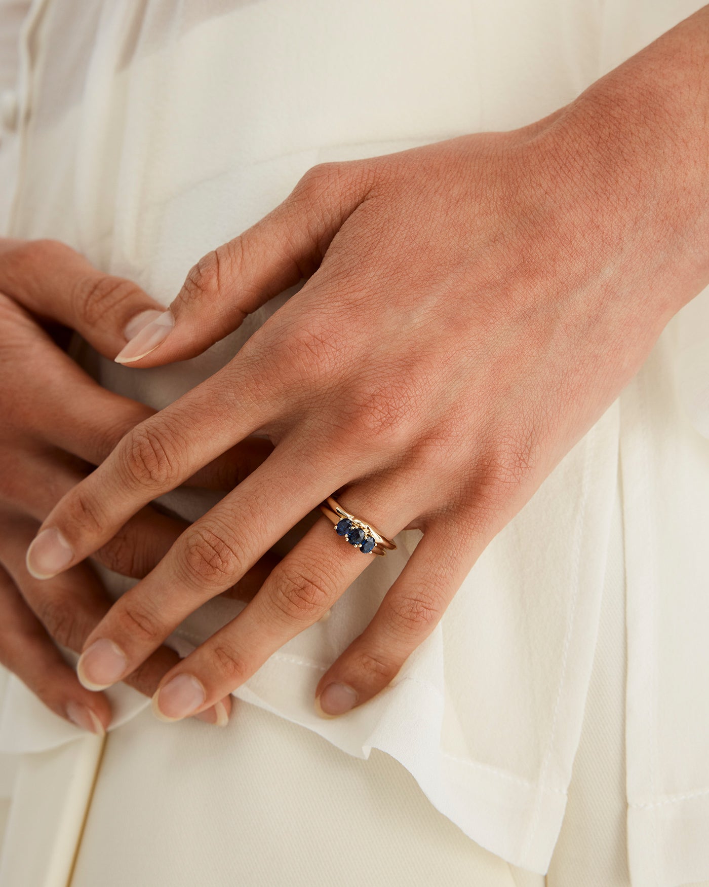 Woman wearing a engagement ring with three oval sapphire stones.