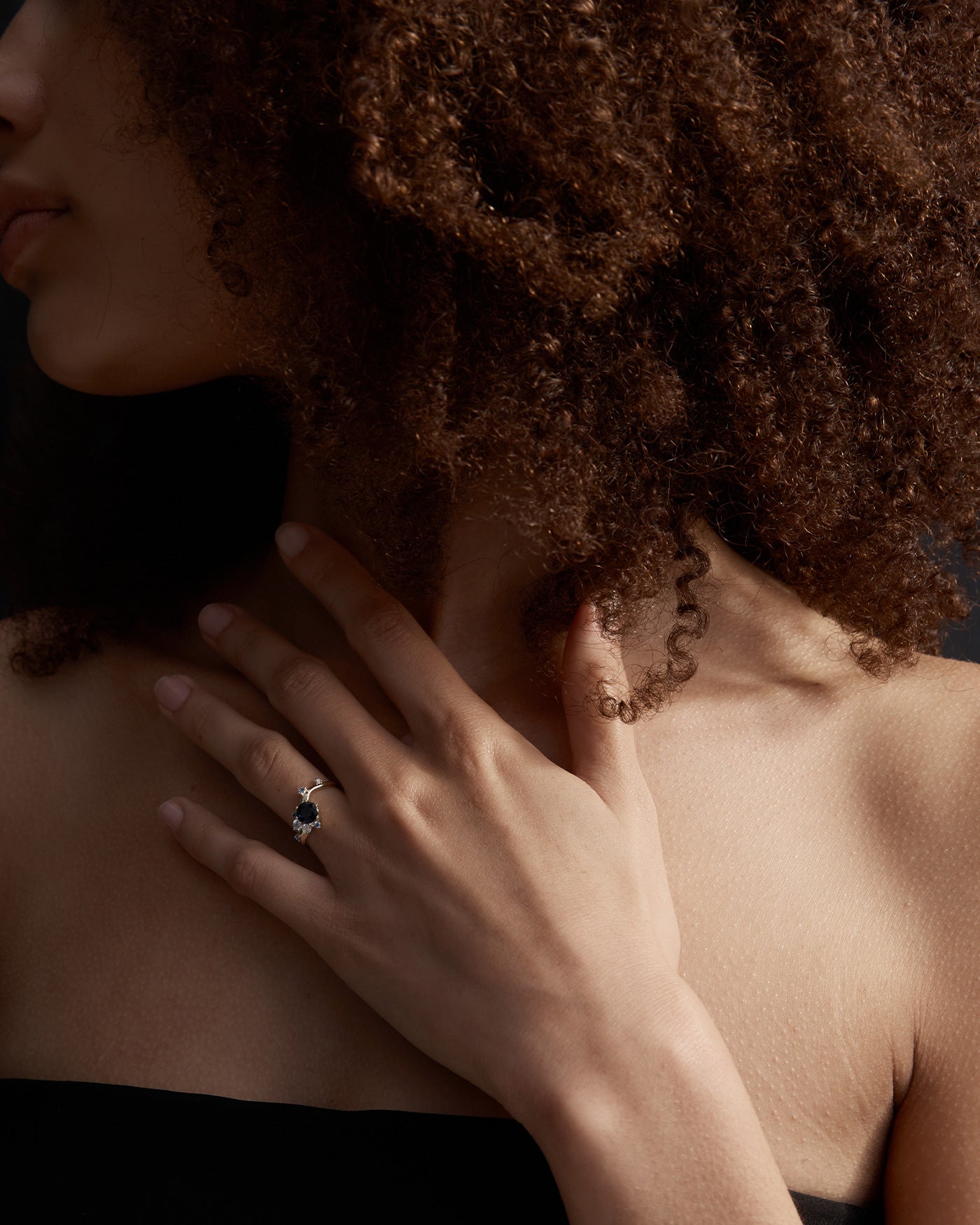 woman wearing a yellow gold engagement ring with a cluster of laboratory grow diamonds and a centre sapphire stone