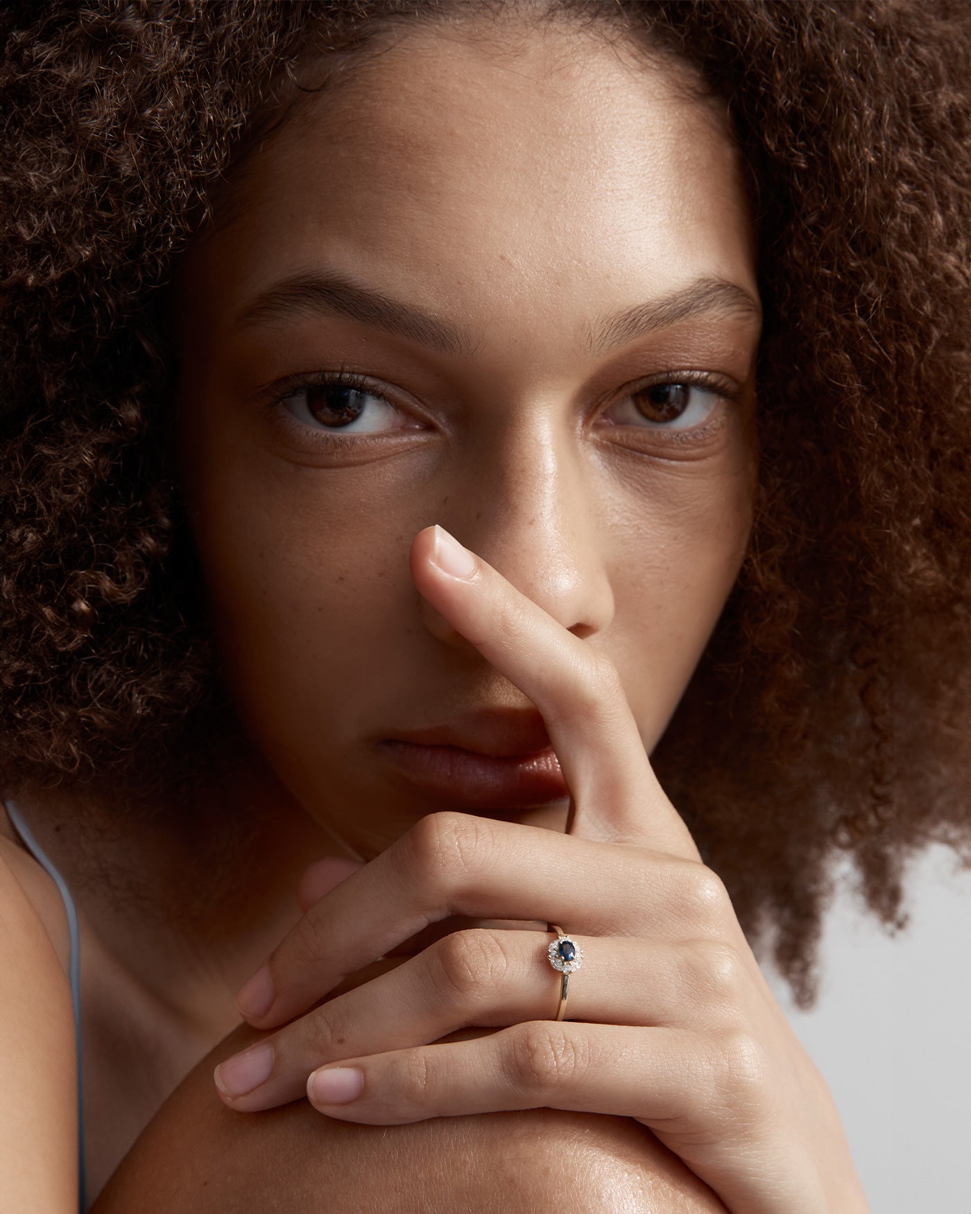 Woman wearing the Tilly Halo Ring with a saphire stone and halo of white diamonds