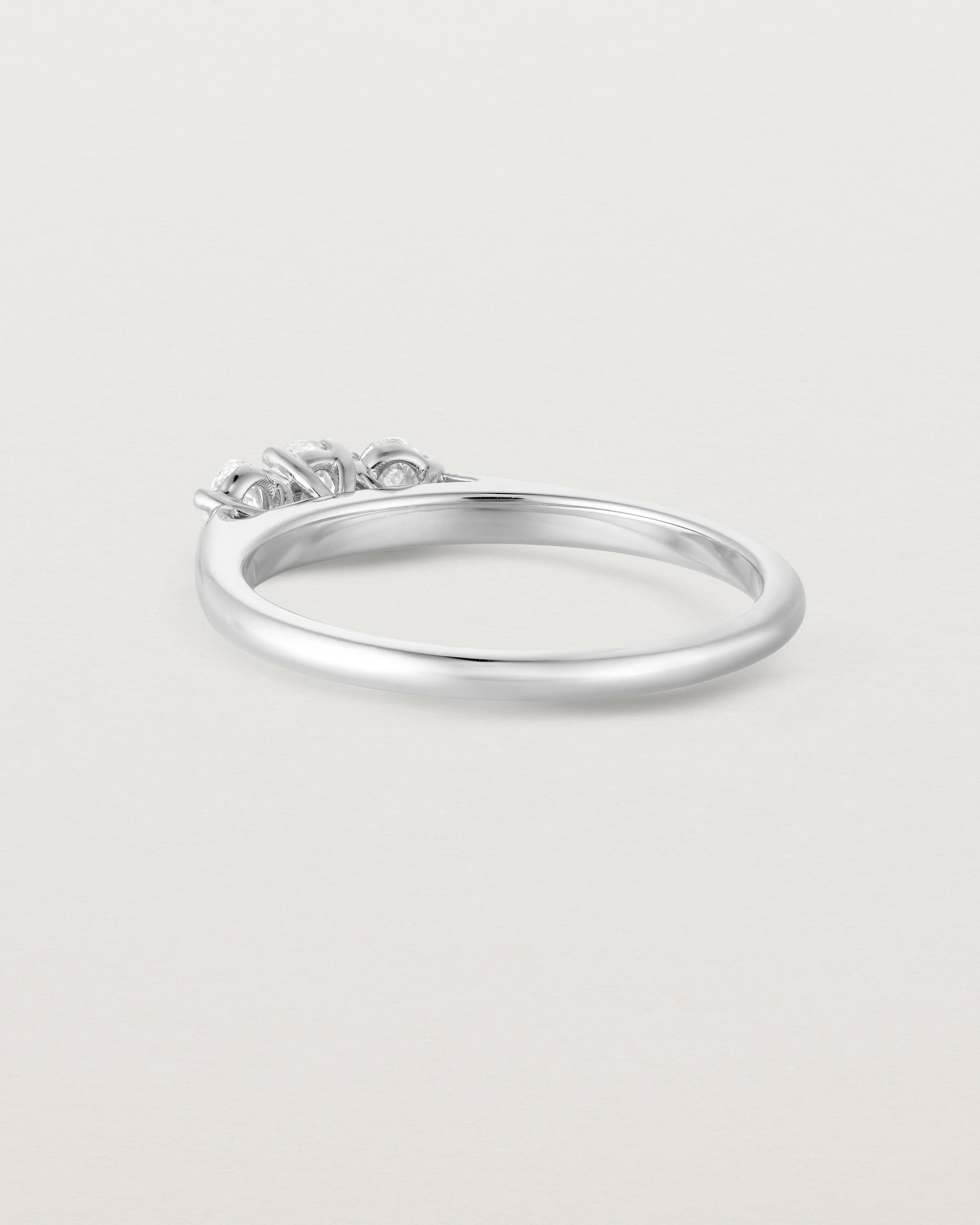 Back facing deep etched image of a white gold engagement ring with three oval white laboratory grown diamonds.