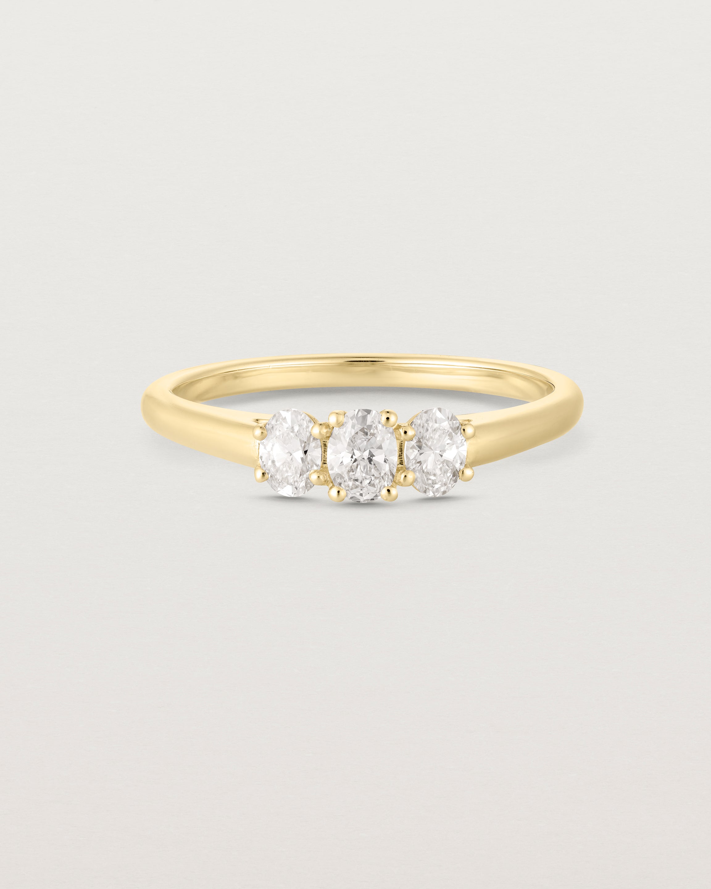 Front on deep etched image of a yellow gold engagement ring with three oval laboratory grown diamonds.