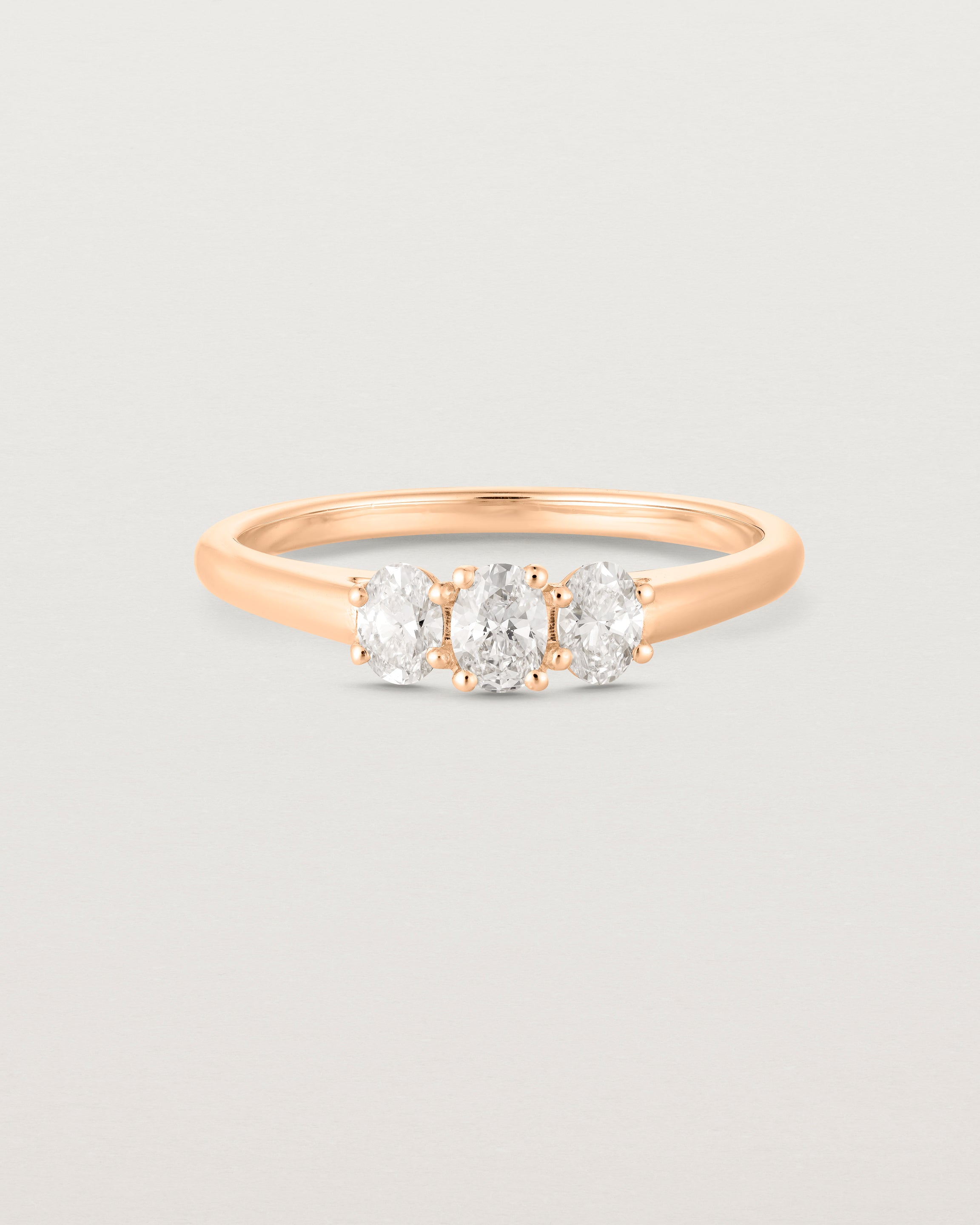 Front on deep etched image of a rose gold engagement ring with three oval white diamonds.