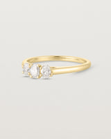 Side facing deep etched image of a yellow gold engagement ring with three oval diamonds.