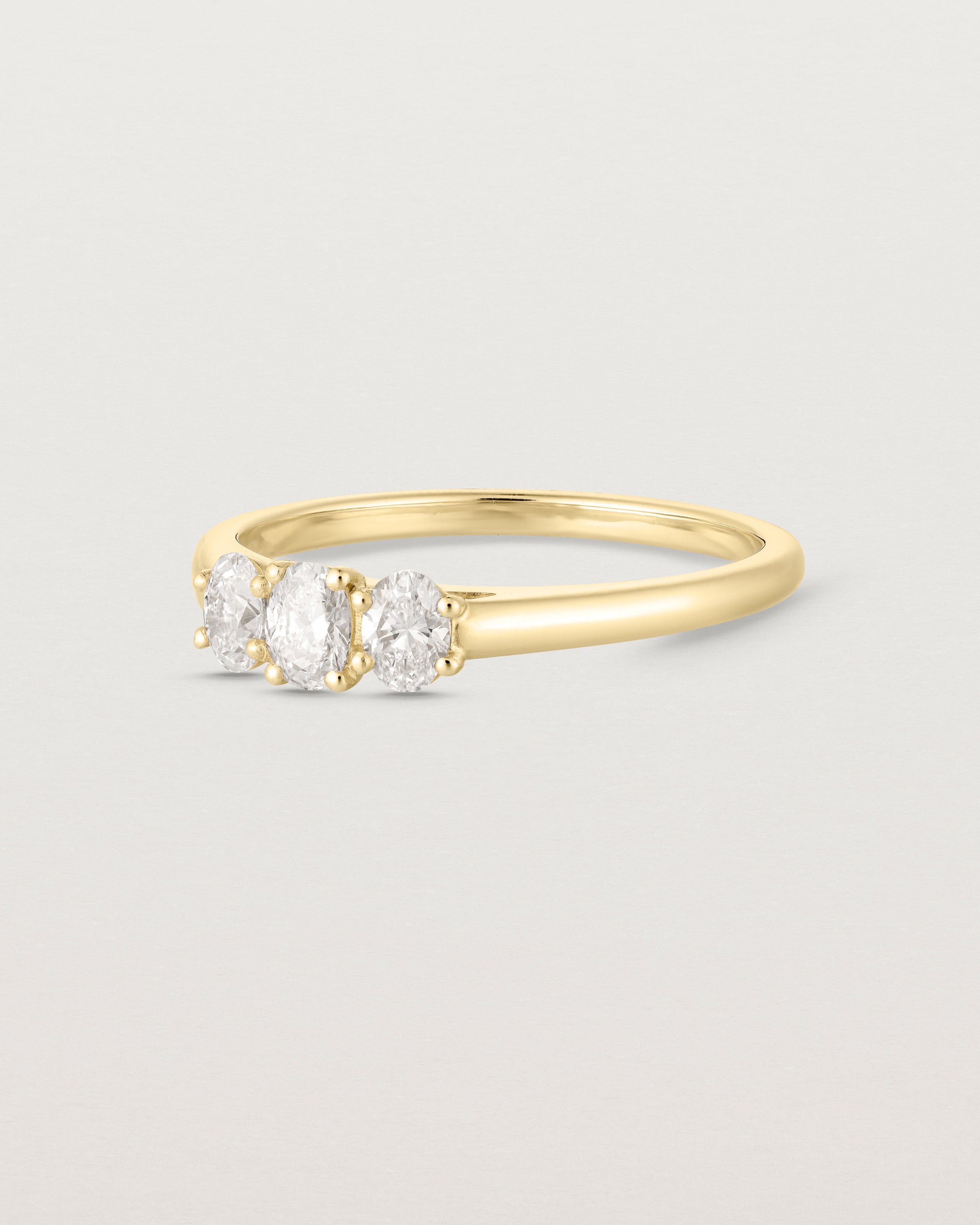 Side facing deep etched image of a yellow gold engagement ring with three oval laboratory grown diamonds.