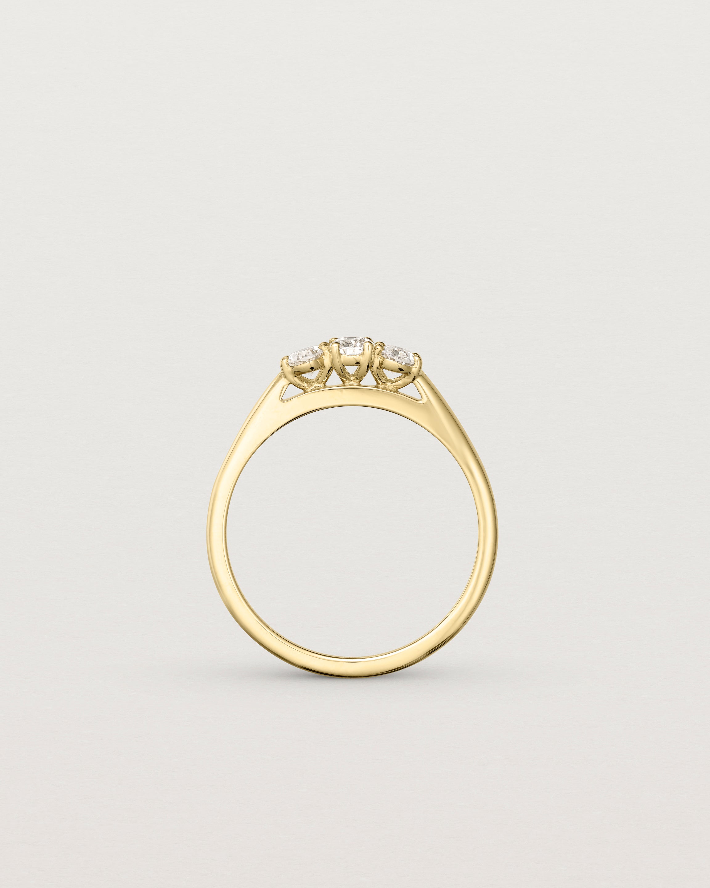 Standing  deep etched image of a yellow gold engagement ring with three oval laboratory grown diamonds.