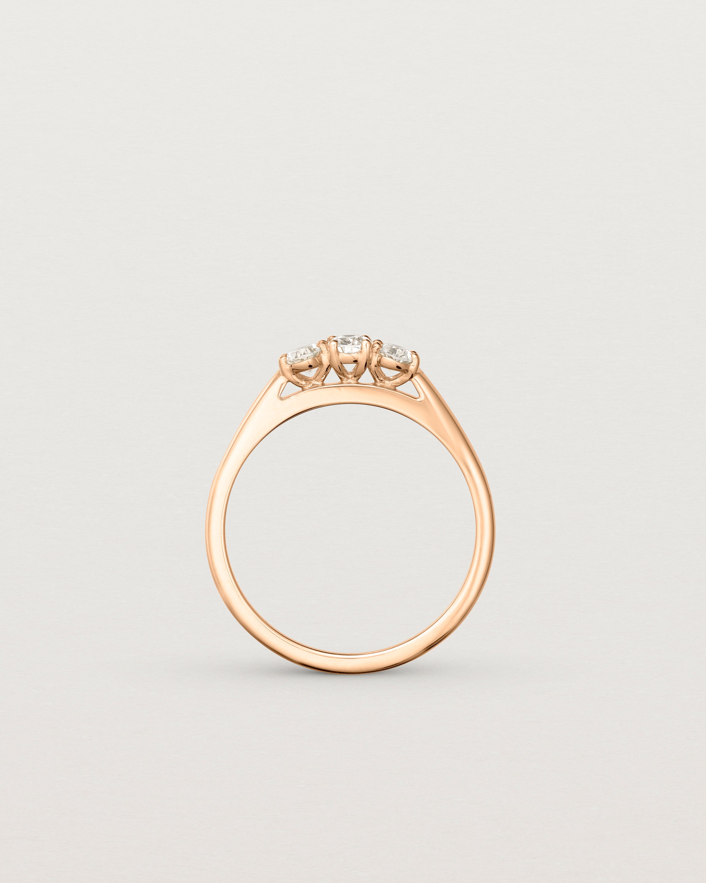 Standing deep etched image of a rose gold engagement ring with three oval white diamonds.