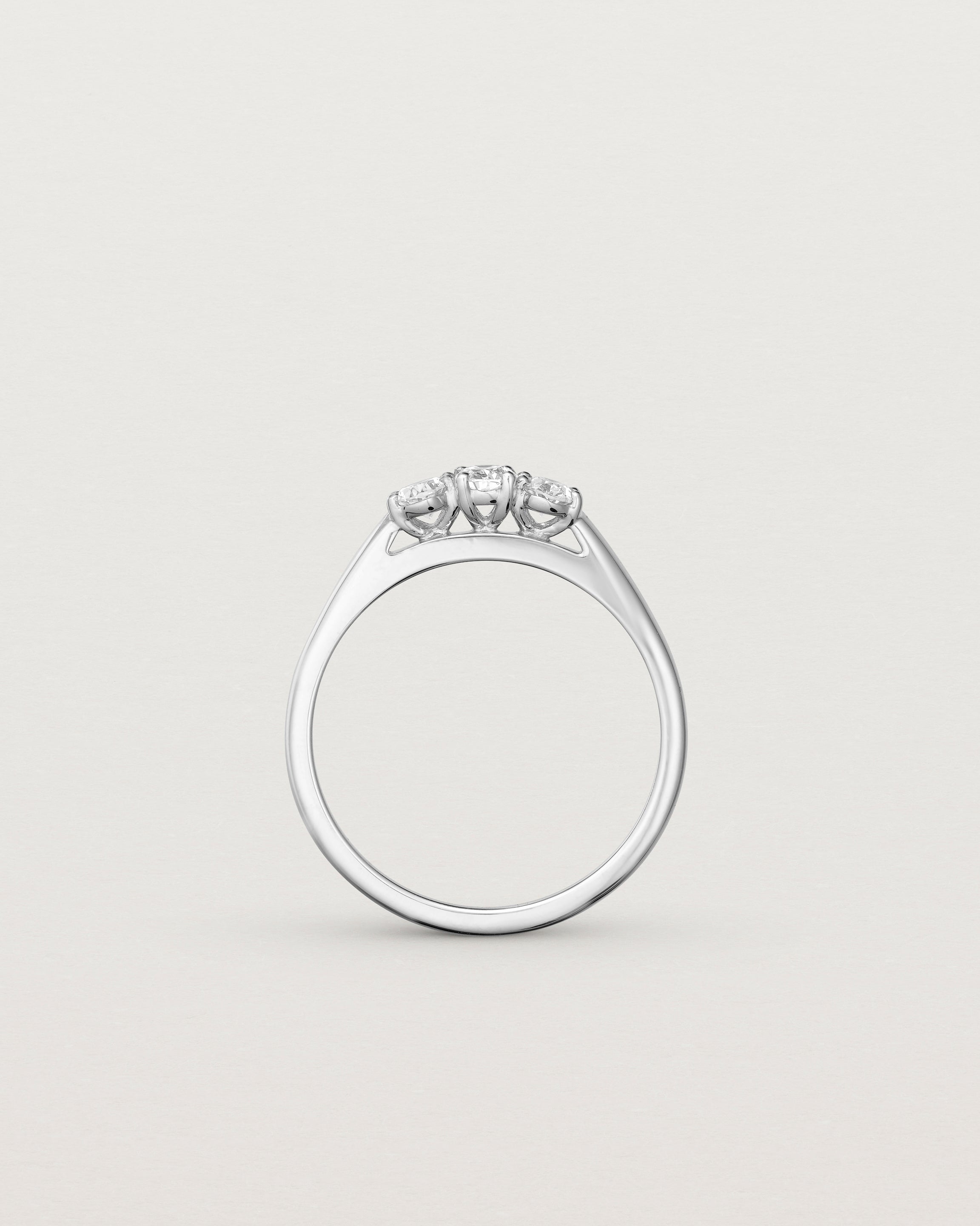 Standing deep etched image of a white gold engagement ring with three oval white laboratory grown diamonds.