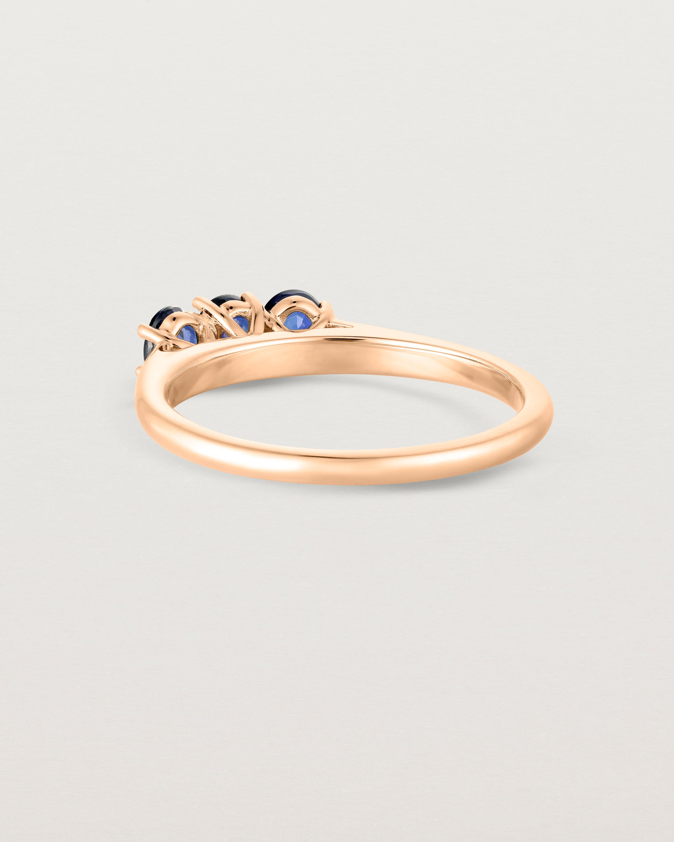 Back facing deep etched image of a rose gold engagement ring with three oval sapphire stones.