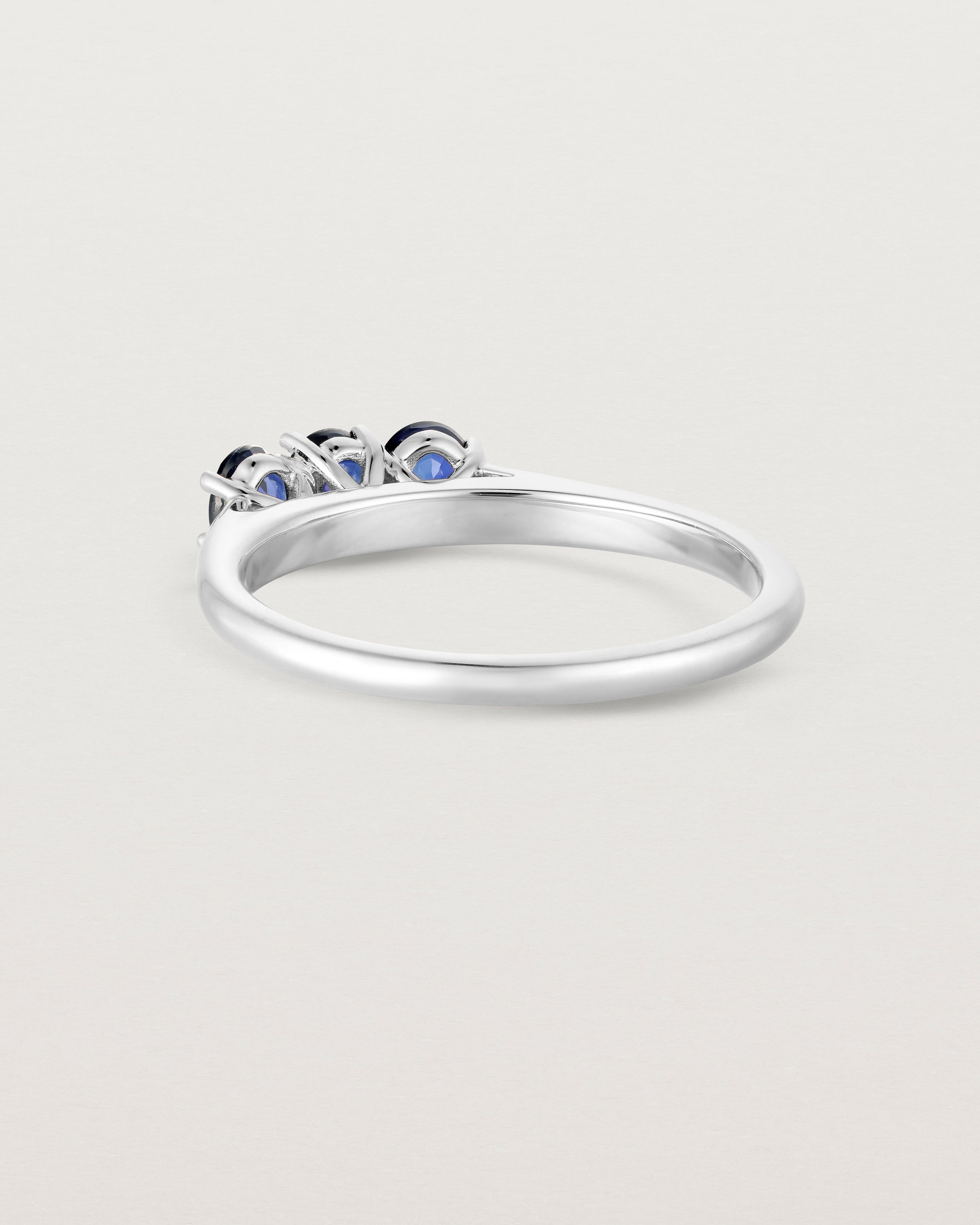 Side facing deep etched image of a white gold engagement ring with three oval sapphire stones.