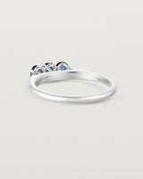 Side facing deep etched image of a white gold engagement ring with three oval sapphire stones.