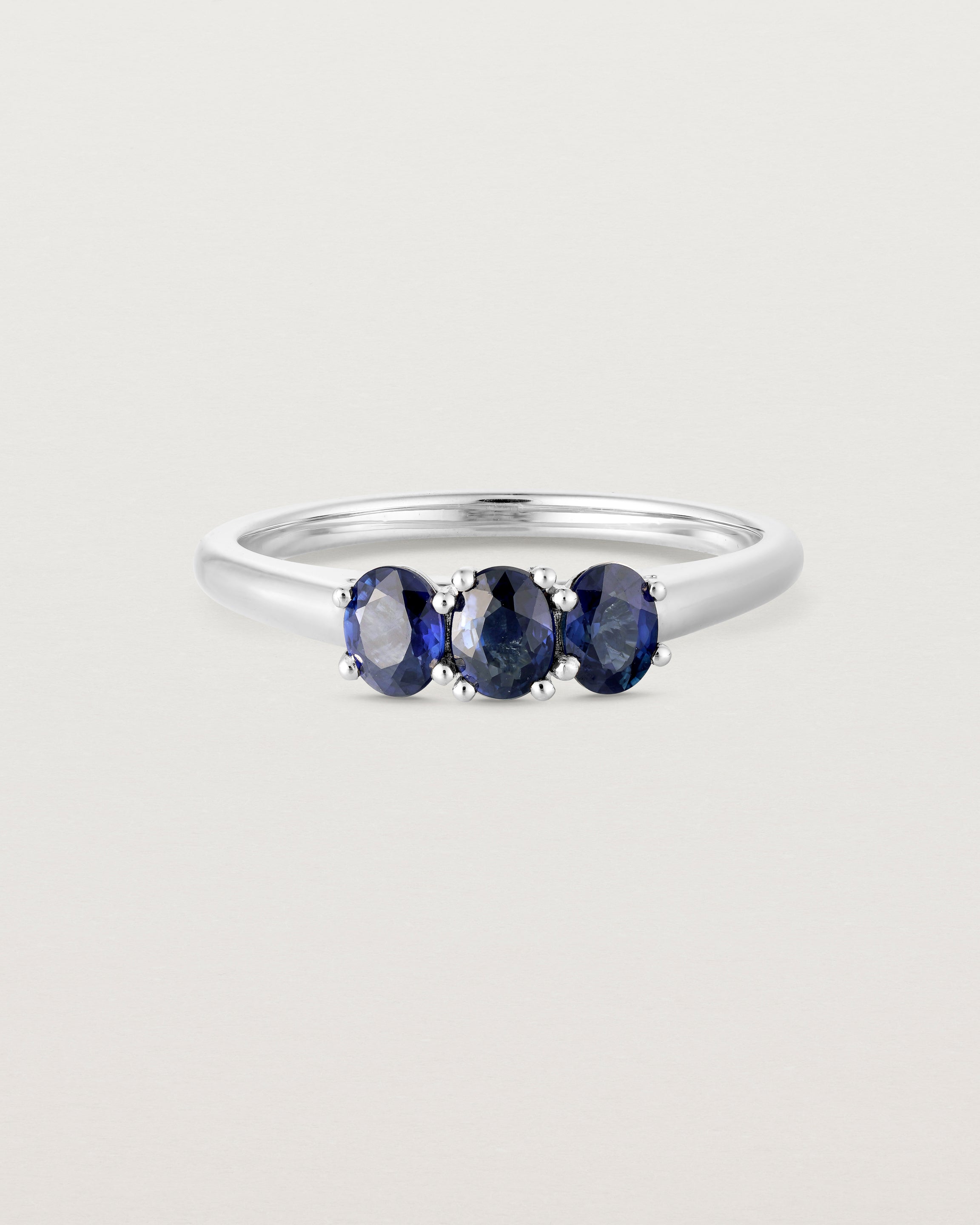 Front on deep etched image of a white gold engagement ring with three oval sapphire stones.