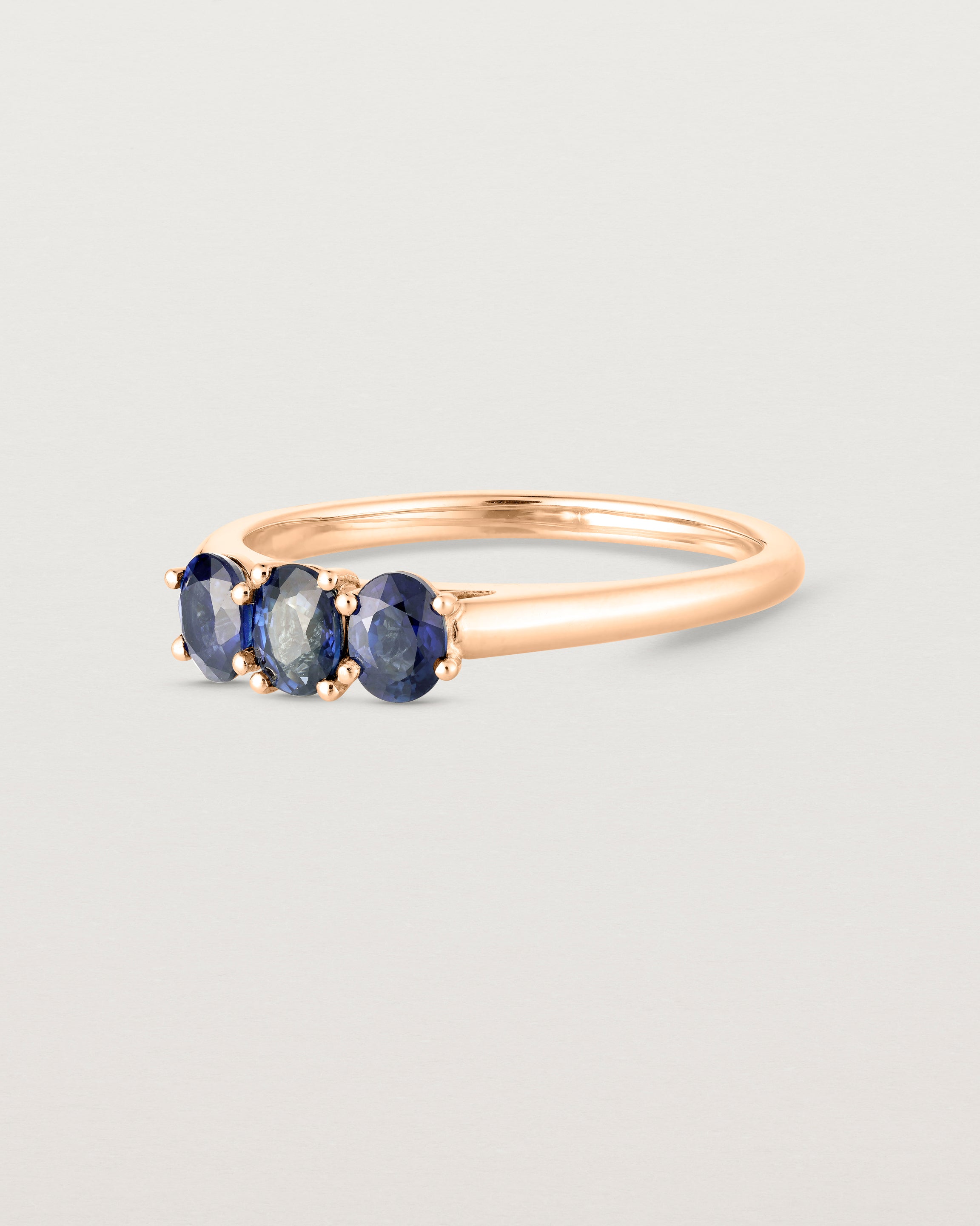 Side on deep etched image of a rose gold engagement ring with three oval sapphire stones.