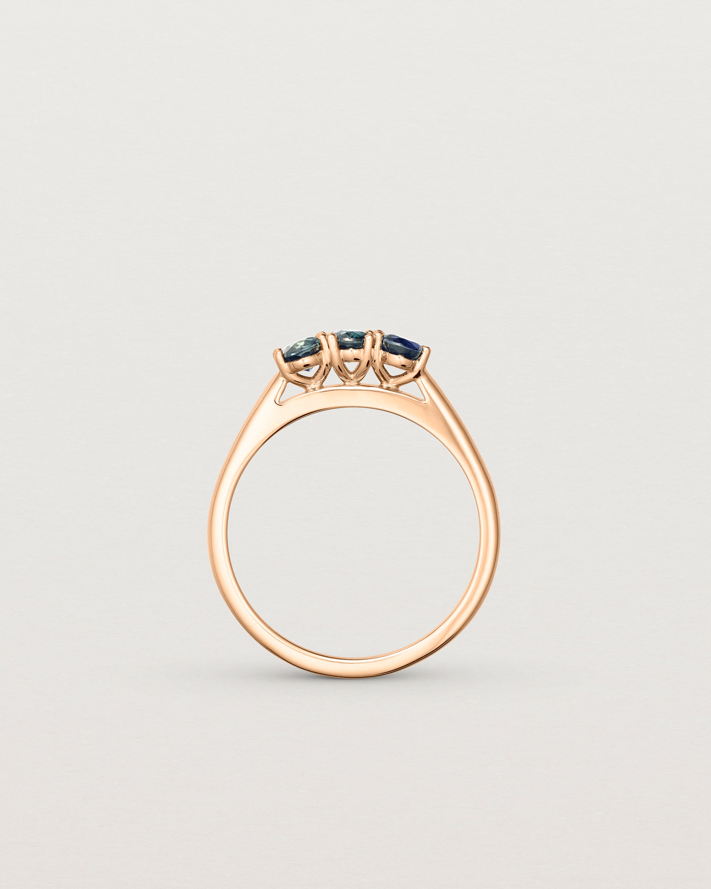 Standing deep etched image of a rose gold engagement ring with three oval sapphire stones.