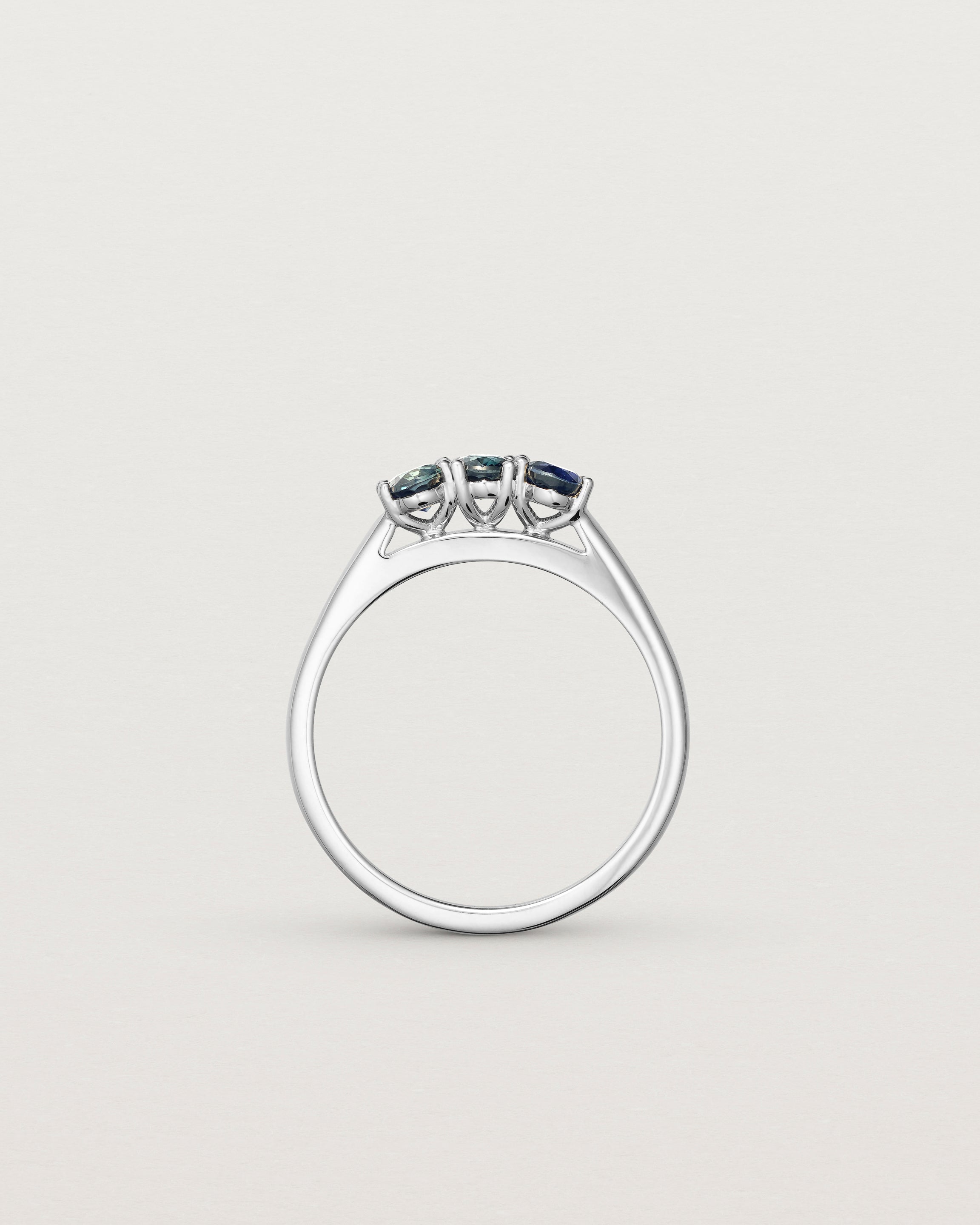 Standing deep etched image of a white gold engagement ring with three oval sapphire stones.