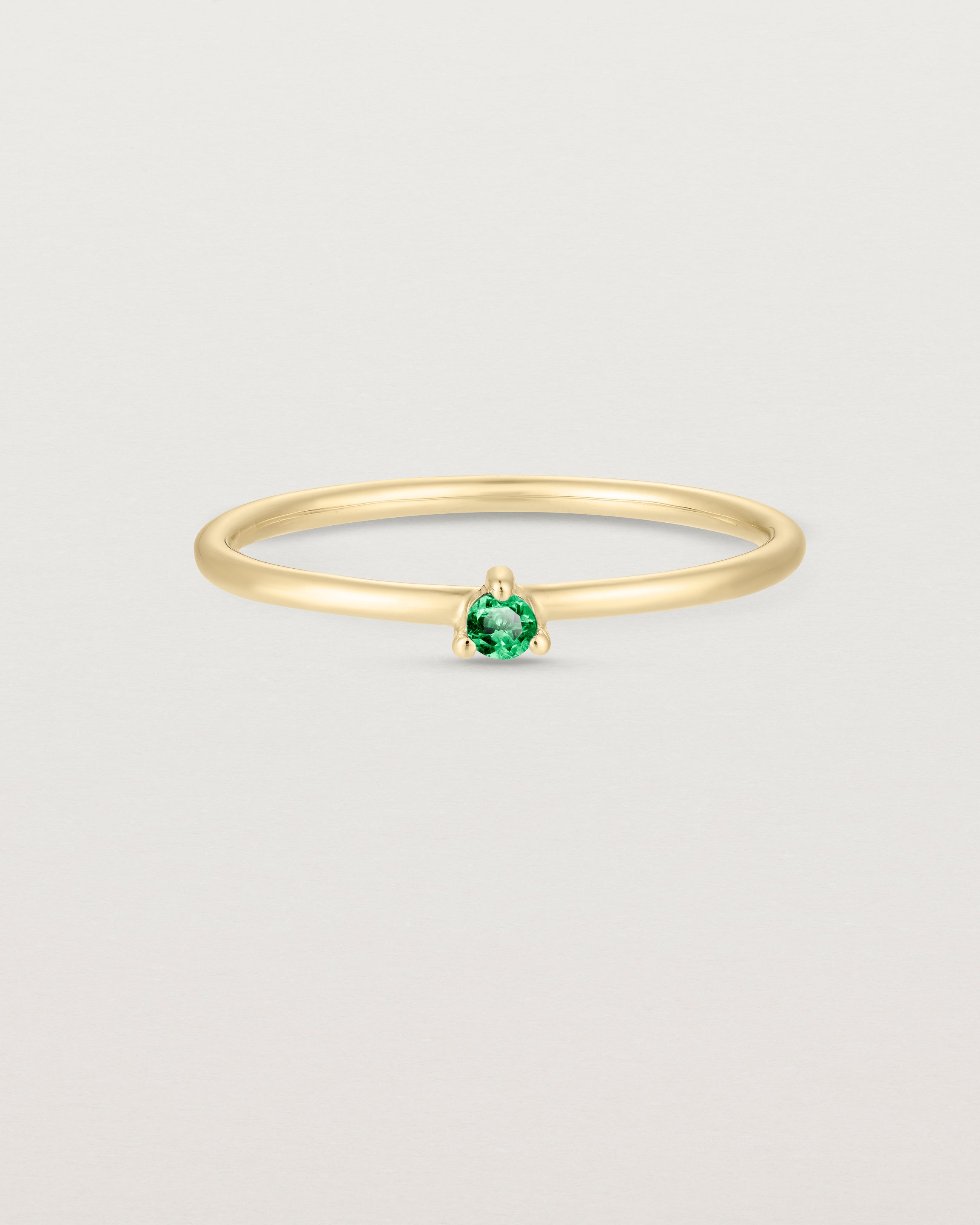 Front facing deep etched image of a yellow gold ring with an emerald birthstone.