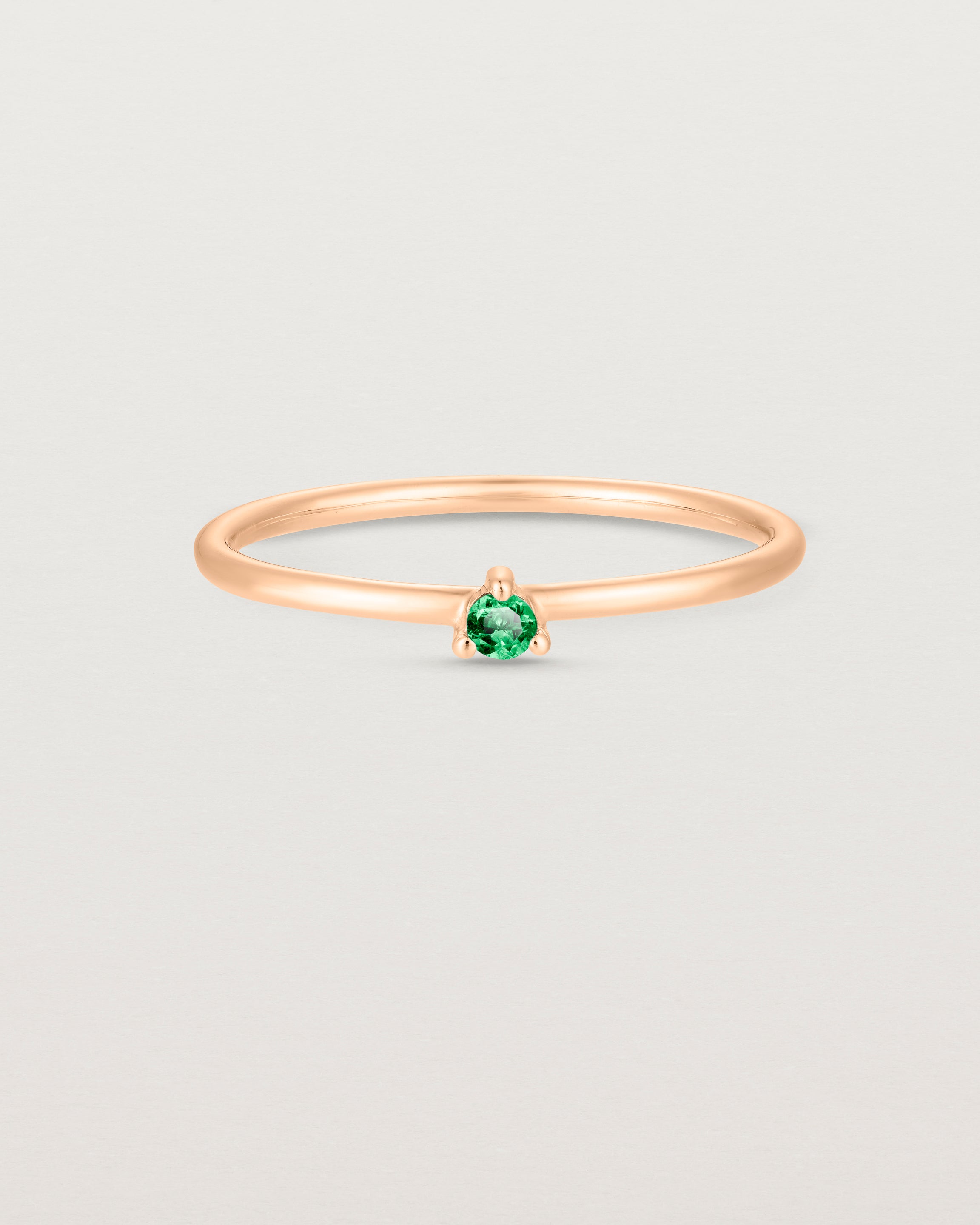 Front facing deep etched image of a rose gold ring with an emerald birthstone.