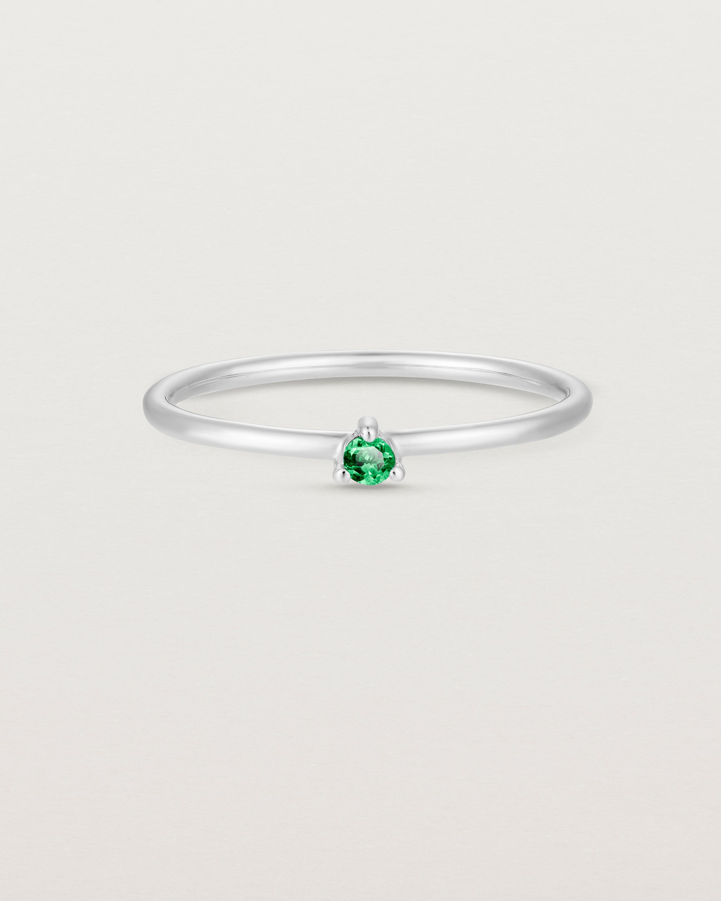 Front facing deep etched image of a white gold ring with an emerald birthstone.