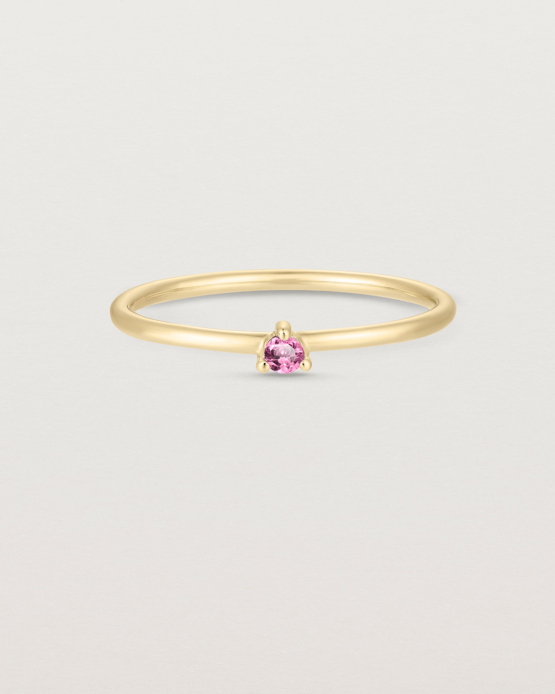 Front facing deep etched image of a yellow gold ring with a pink tourmaline birthstone.