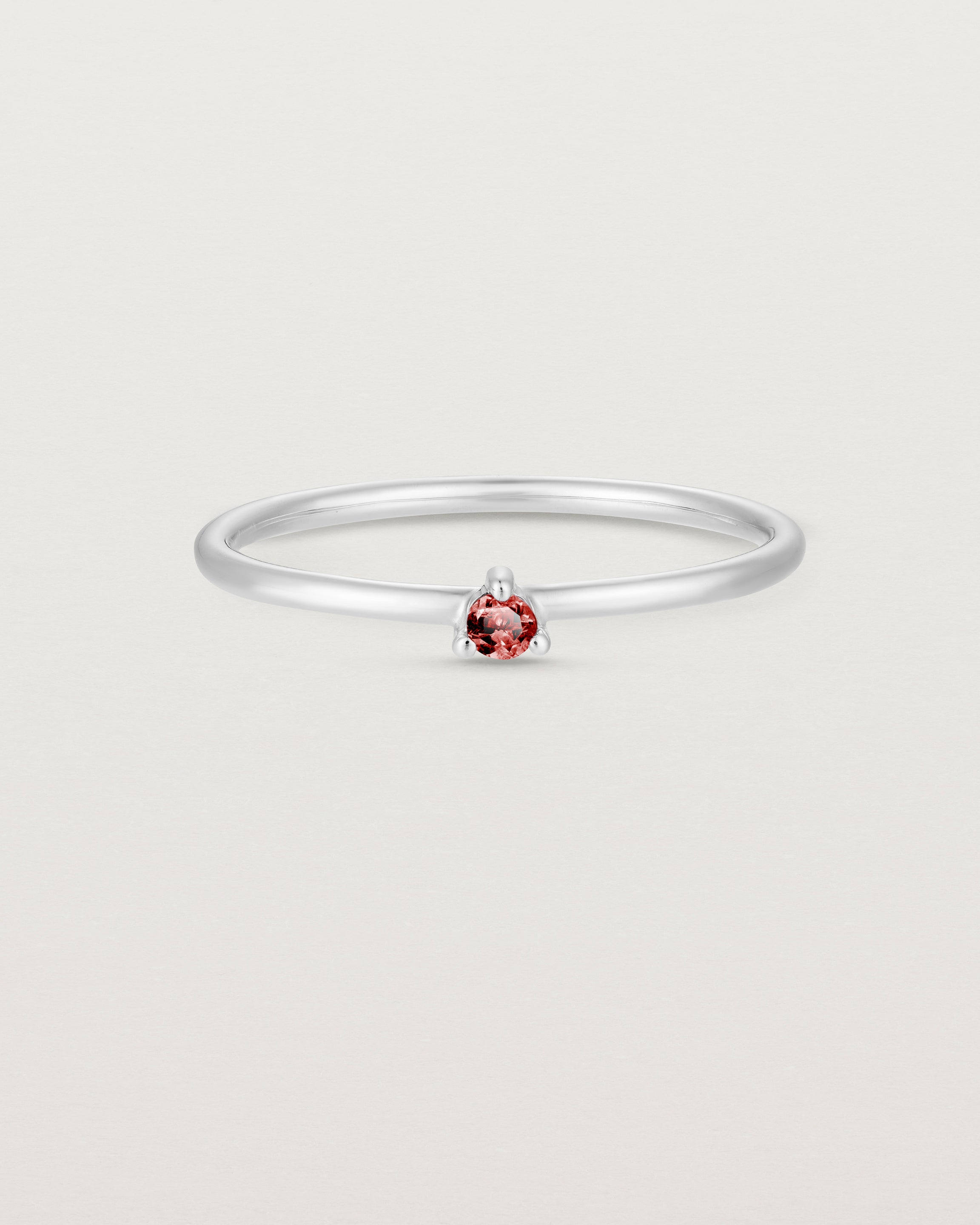 Front facing deep etched image of a white gold ring with a ruby birthstone.