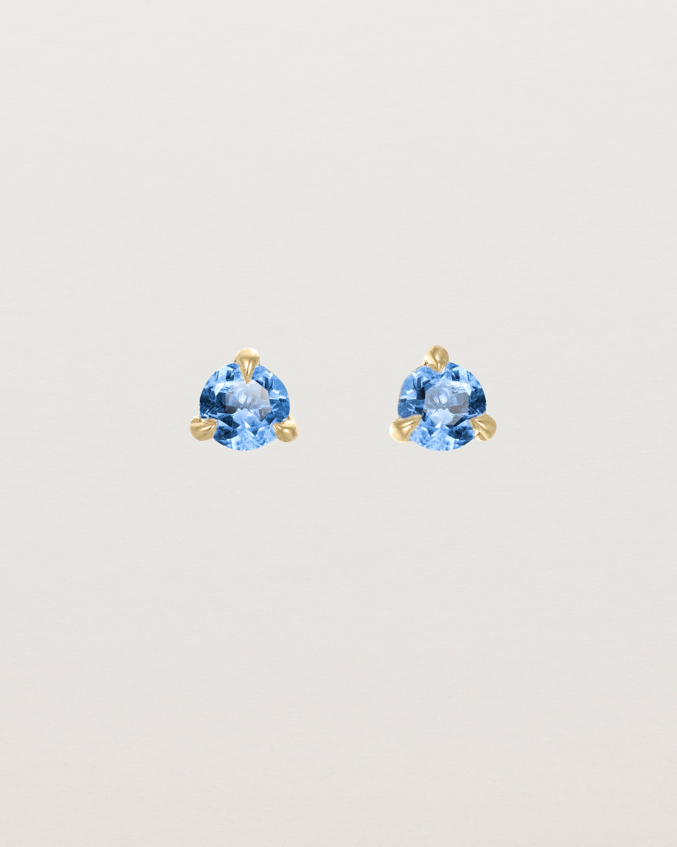 Front facing deep etched image of a pair of yellow gold earrings with a blue topaz birthstone.