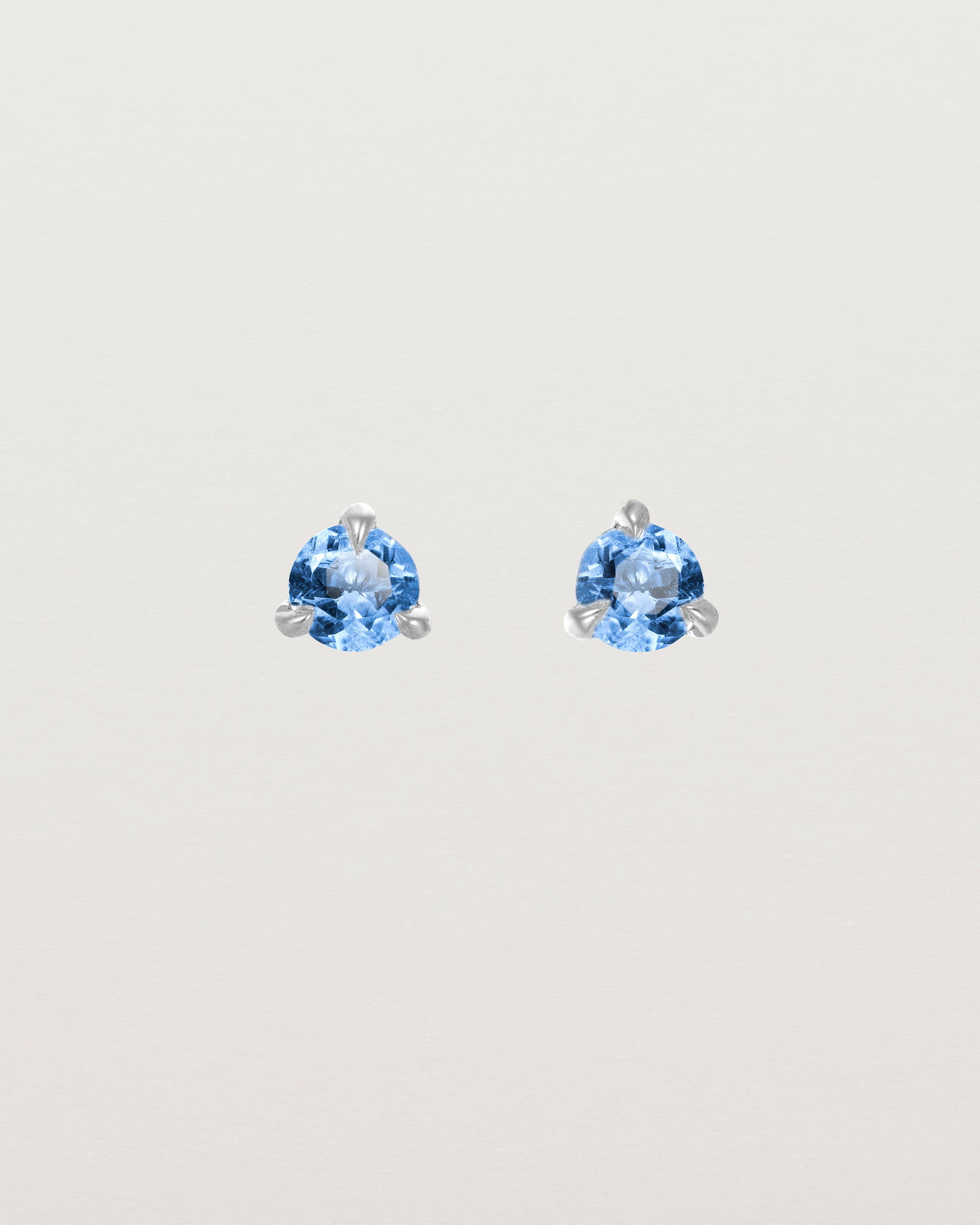 Front facing deep etched image of a pair of white gold earrings with a blue topaz birthstone.