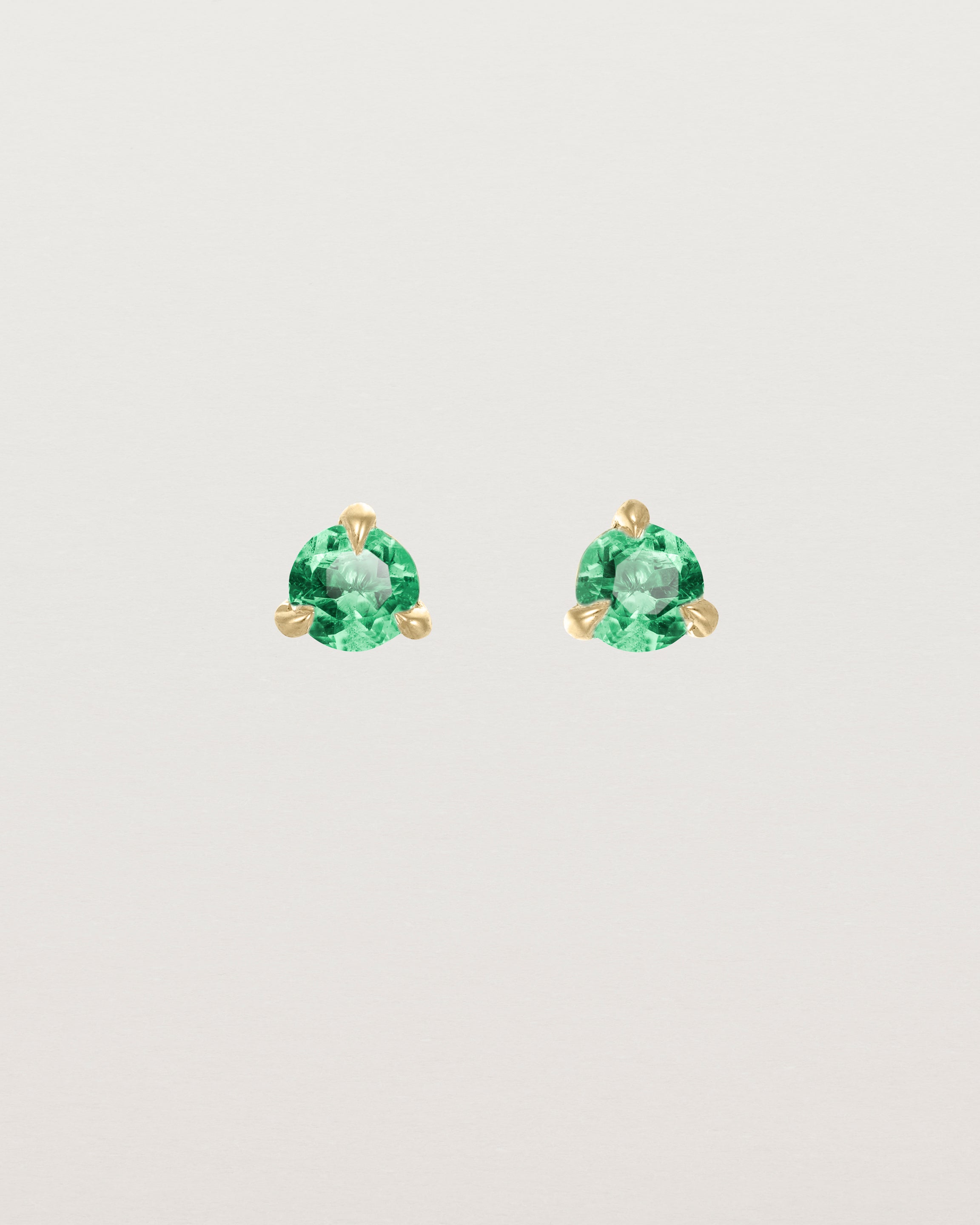 Front facing deep etched image of a pair of yellow gold earrings with an emerald birthstone.