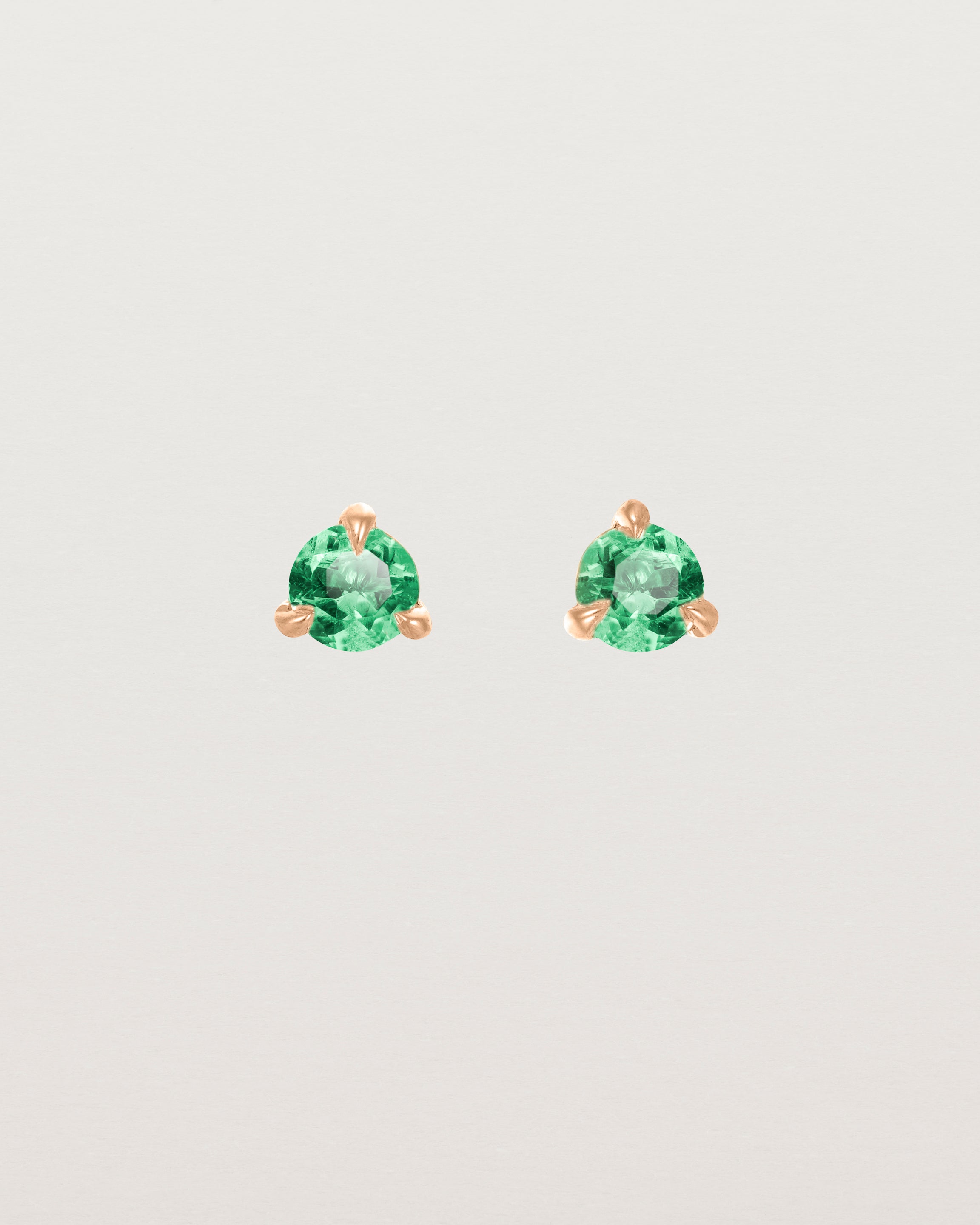 Front facing deep etched image of a pair of rose gold earrings with an emerald birthstone.