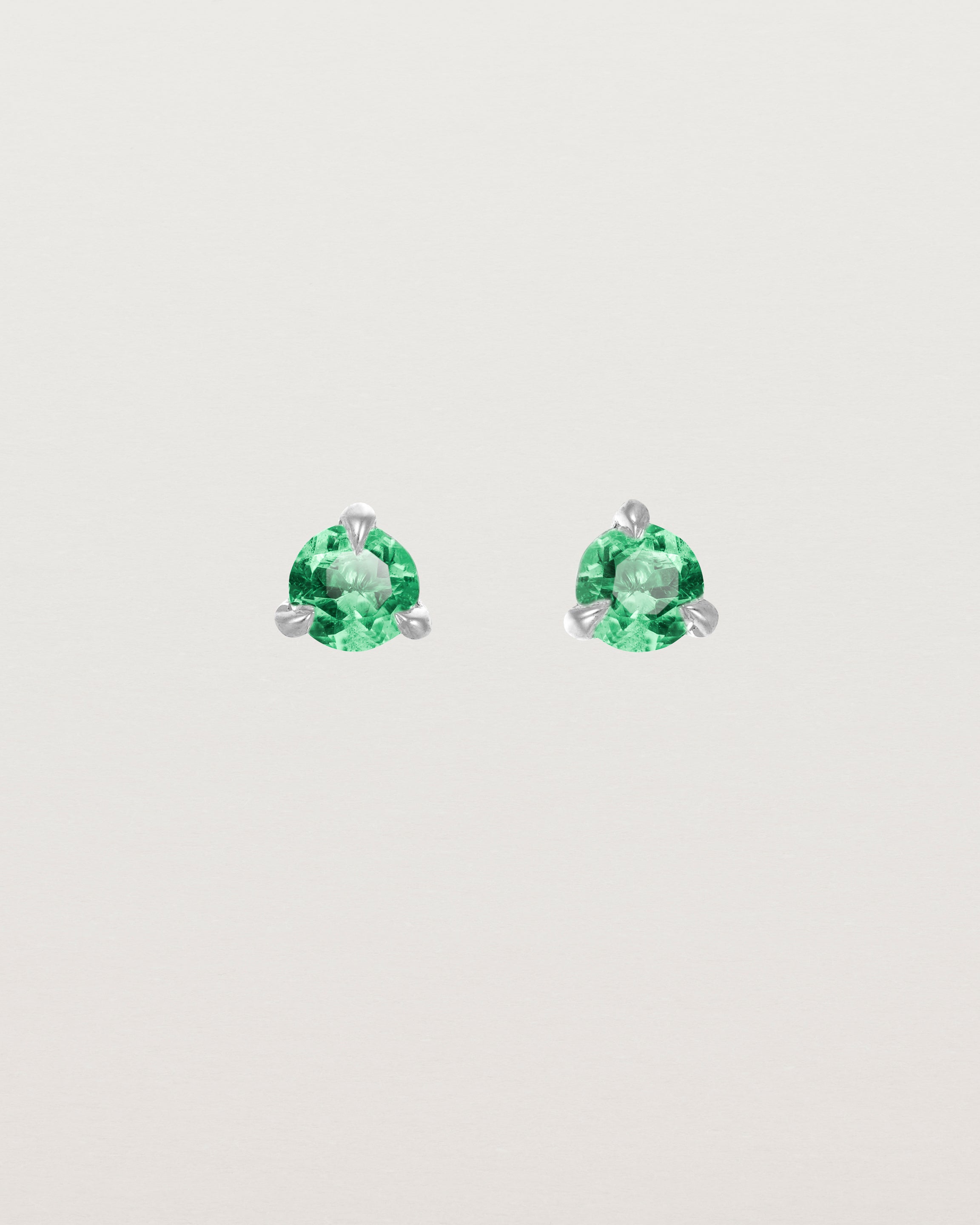 Front facing deep etched image of a pair of white gold earrings with an emerald birthstone.