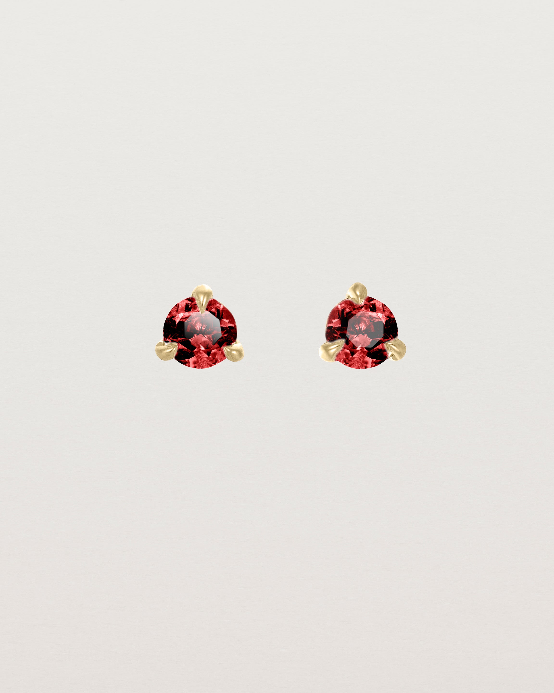 Front facing deep etched image of a pair of yellow gold earrings with a ruby birthstone.