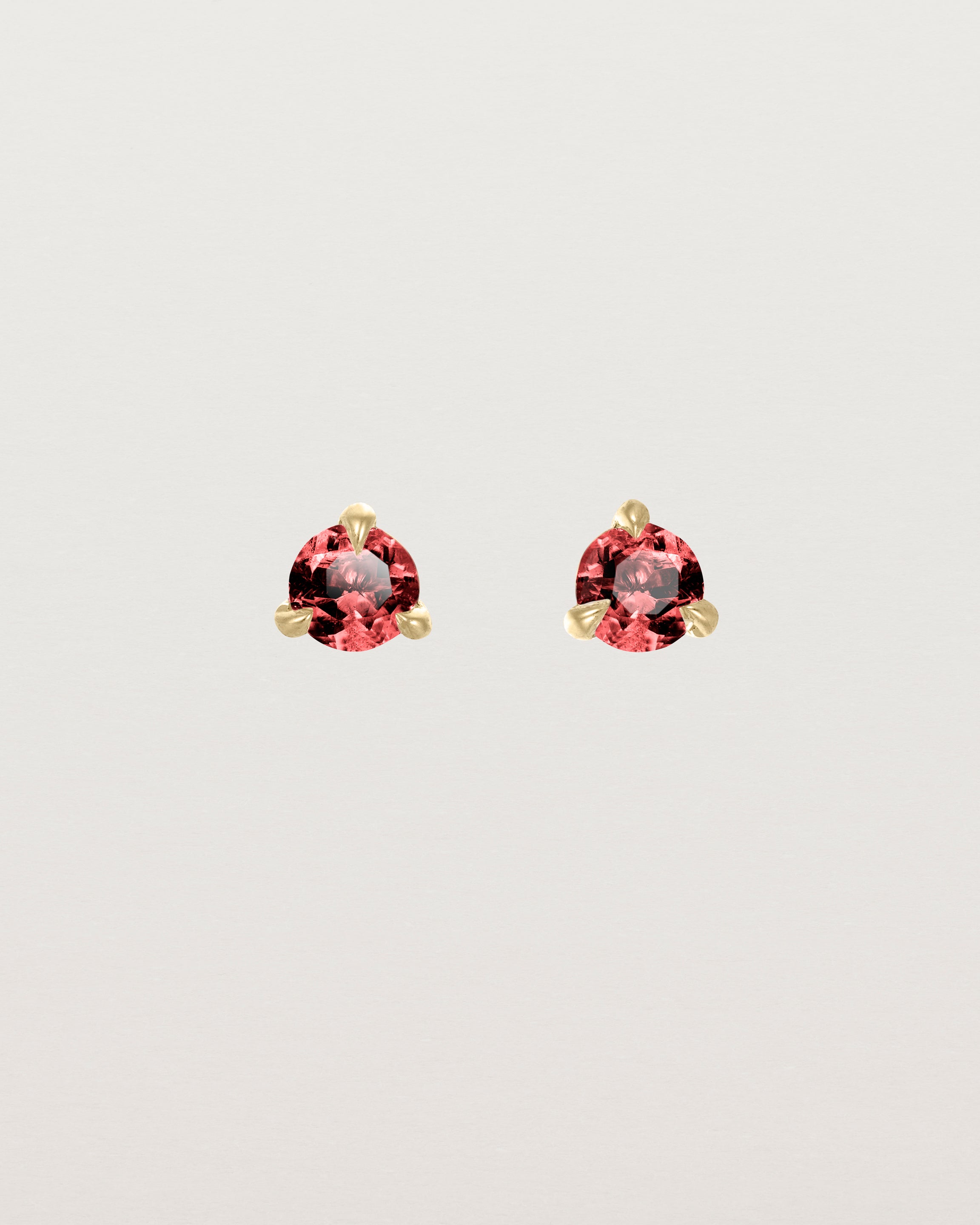 Front facing deep etched image of a pair of yellow gold earrings with an garnet birthstone.