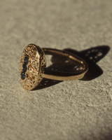 Close up image of a side facing yellow gold vintage inspired shield ring with three Australian sapphires and surrounded by eight old cut white diamonds on flat textured surface.