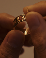 Close up image of a woman holding a yellow gold ring that features a hidden hinge detail, revealing a swallow in flight with a Ceylon sapphire.