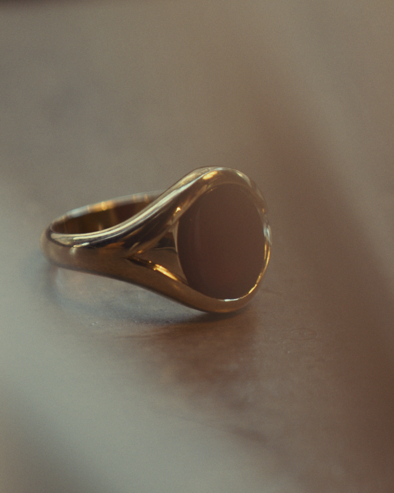 Close up image of a side facing yellow gold signet ring with carnelian on a flat surface.