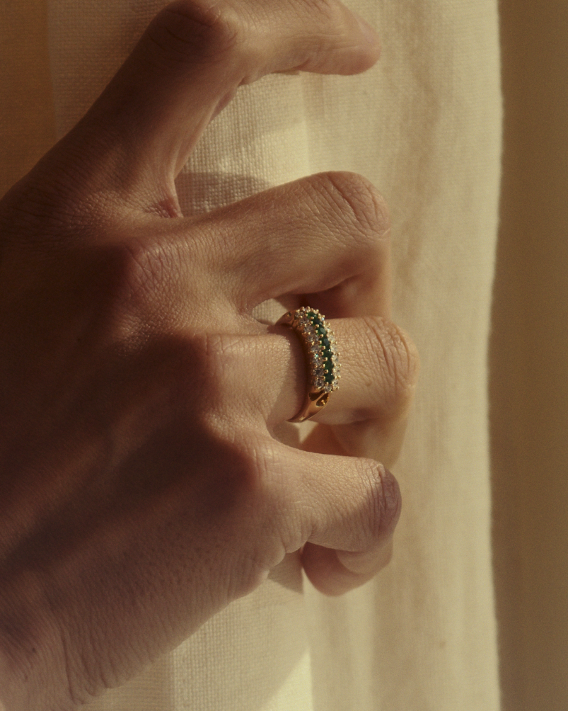 Close up image of a woman wearing a yellow gold vintage inspired wrap ring with seven green emeralds and a graduation of 18 old cut diamonds.