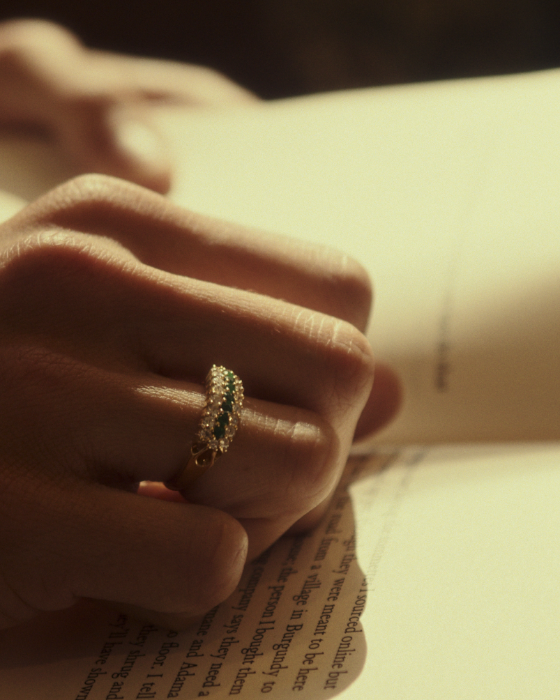 Close up image of a woman wearing a yellow gold vintage inspired wrap ring with seven green emeralds and a graduation of 18 old cut diamonds.