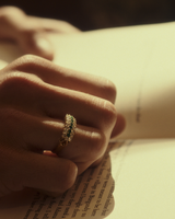 Close up image of a woman wearing a yellow gold vintage inspired wrap ring with seven green emeralds and a graduation of 18 old cut diamonds.