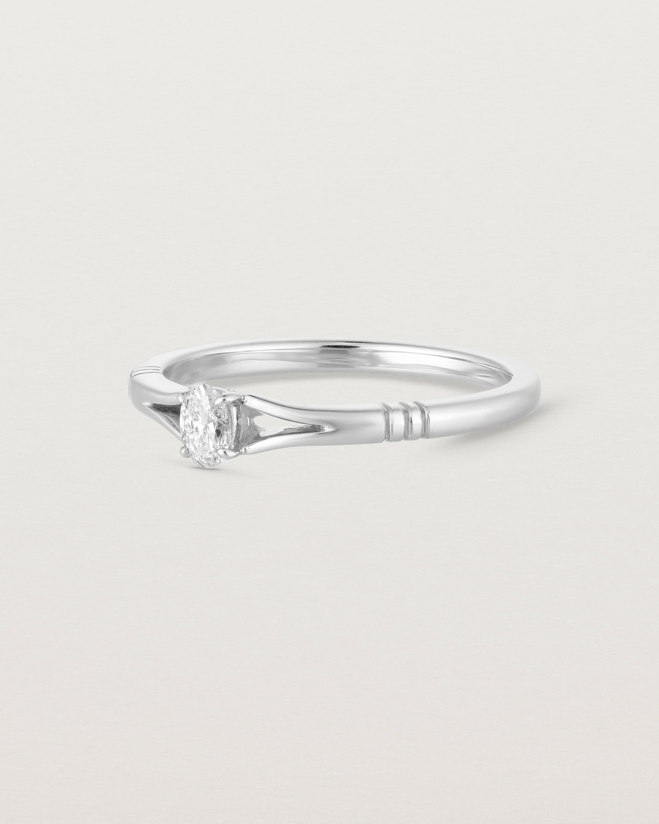 Side facing deep etched image of a white gold engagement ring with an oval diamond.