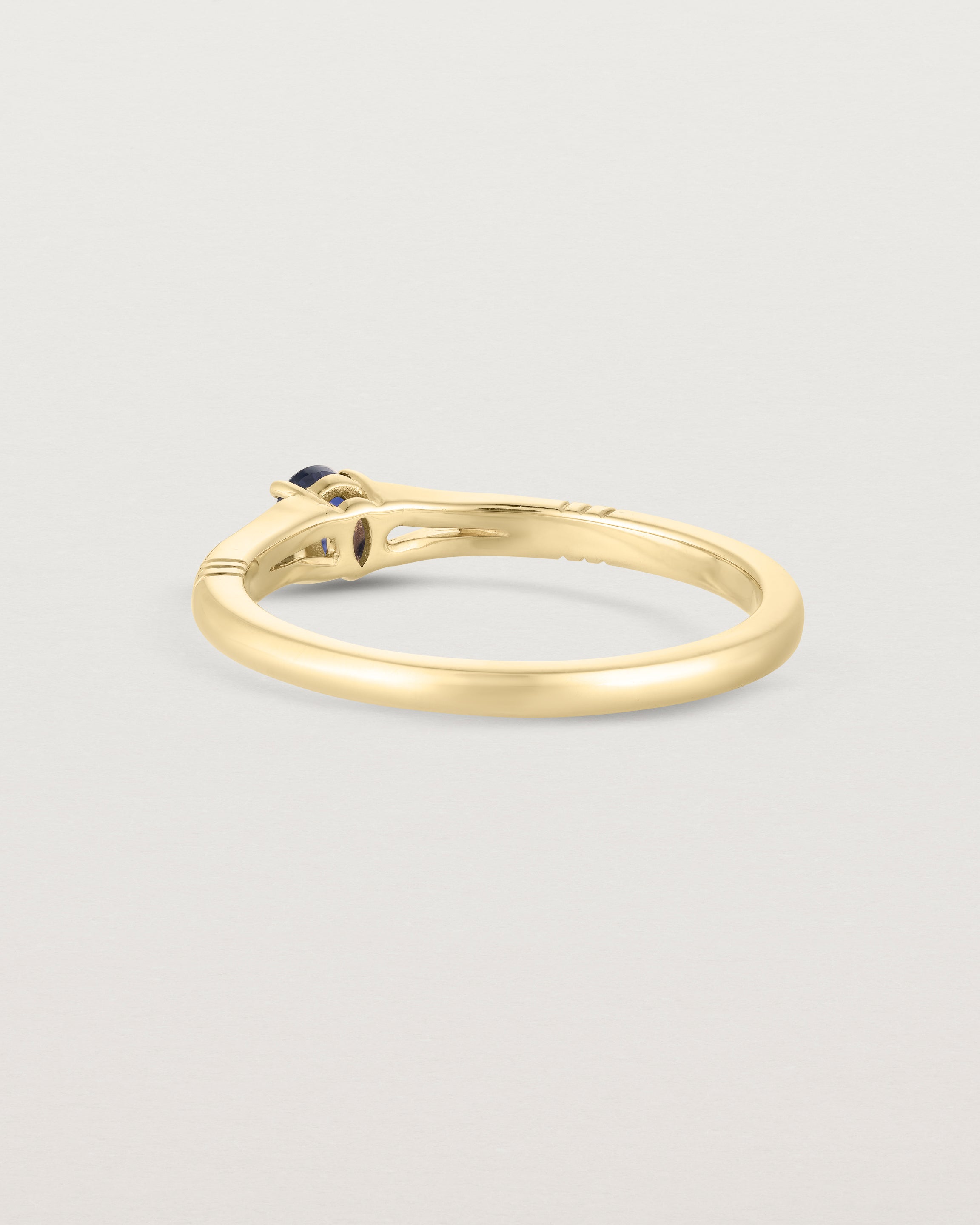 Back facing deep etched image of a yellow gold engagement ring with an oval sapphire stone