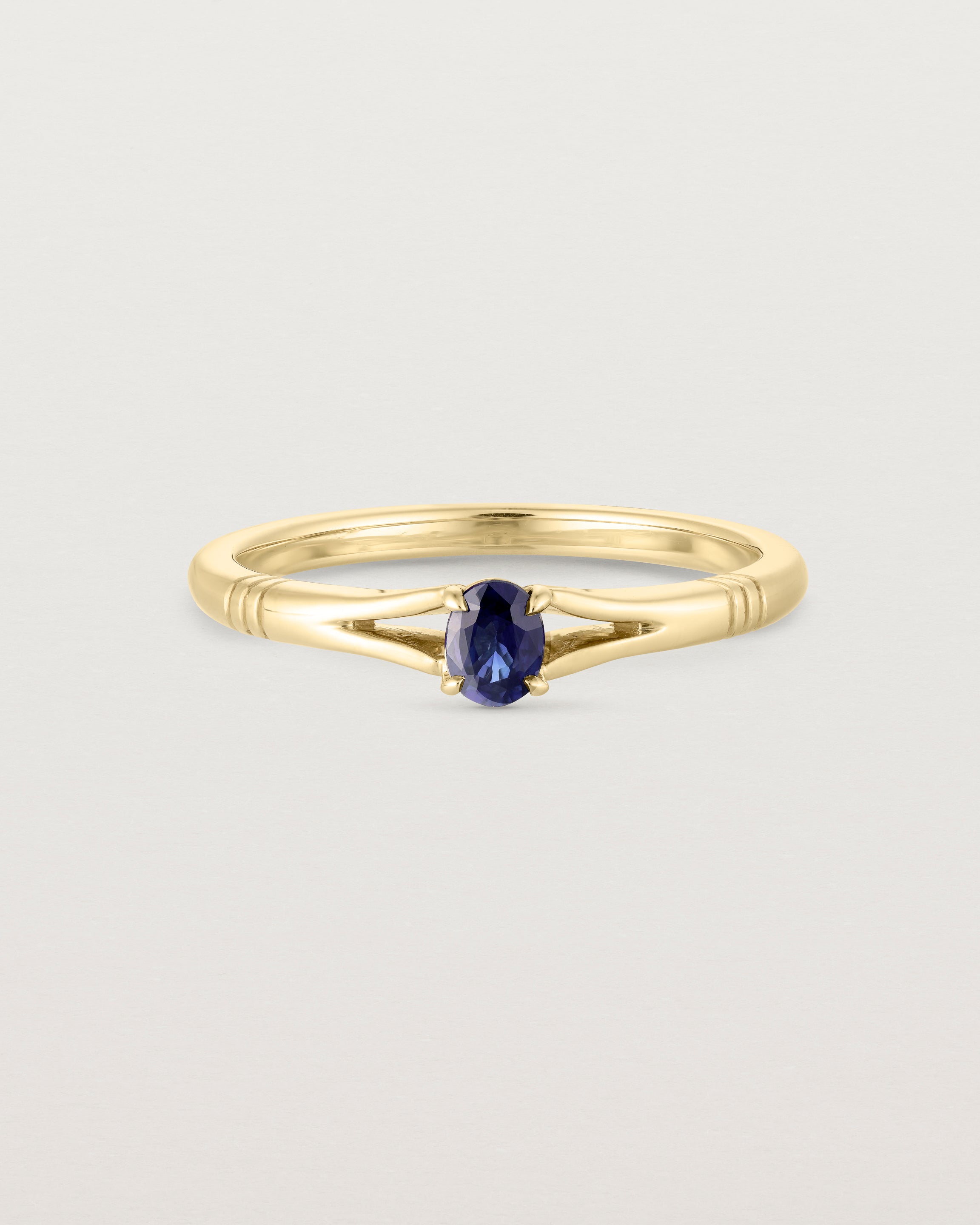 Front on deep etched image of a yellow gold engagement ring with an oval sapphire stone