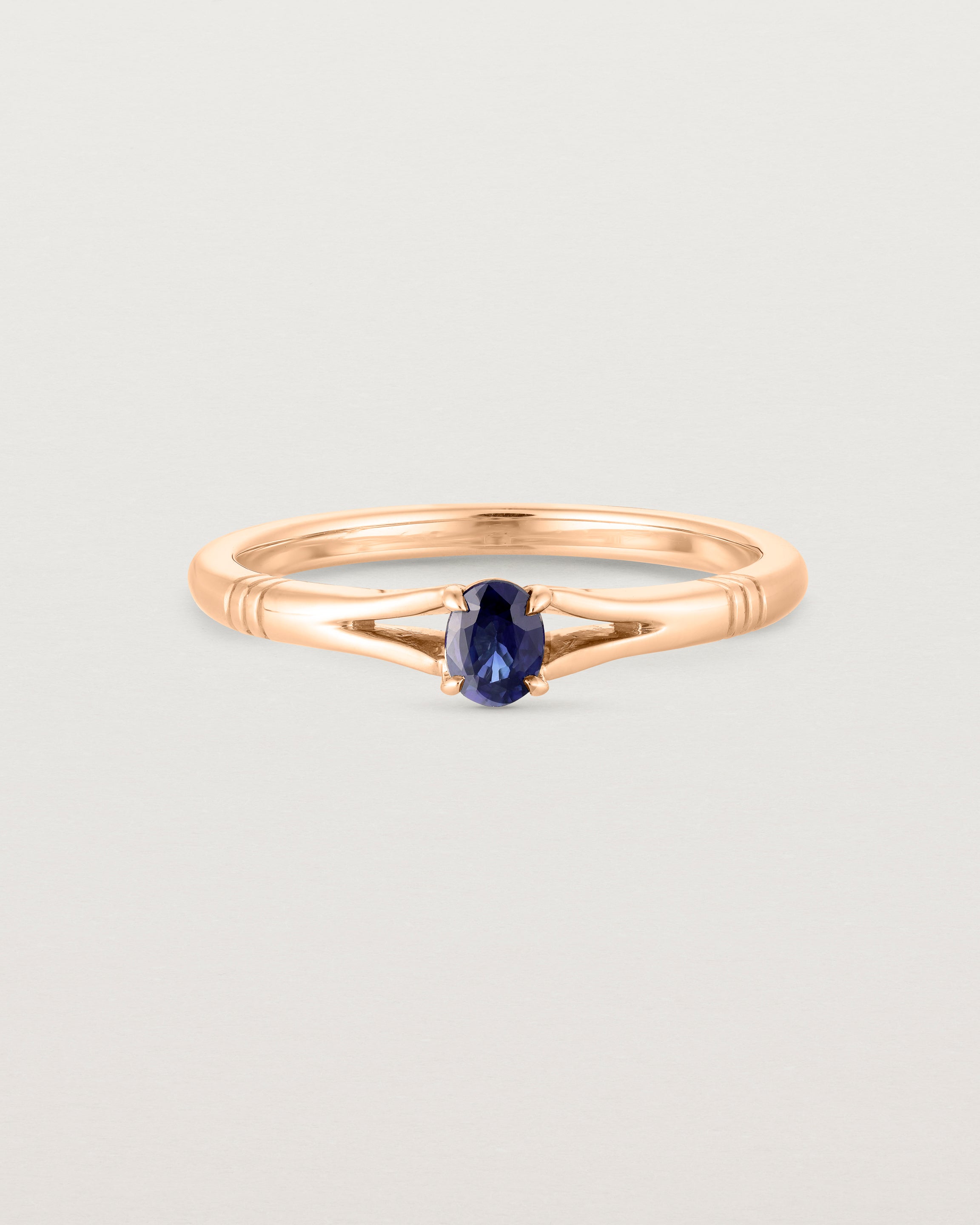 Front on deep etched image of a rose gold engagement ring with an oval sapphire stone