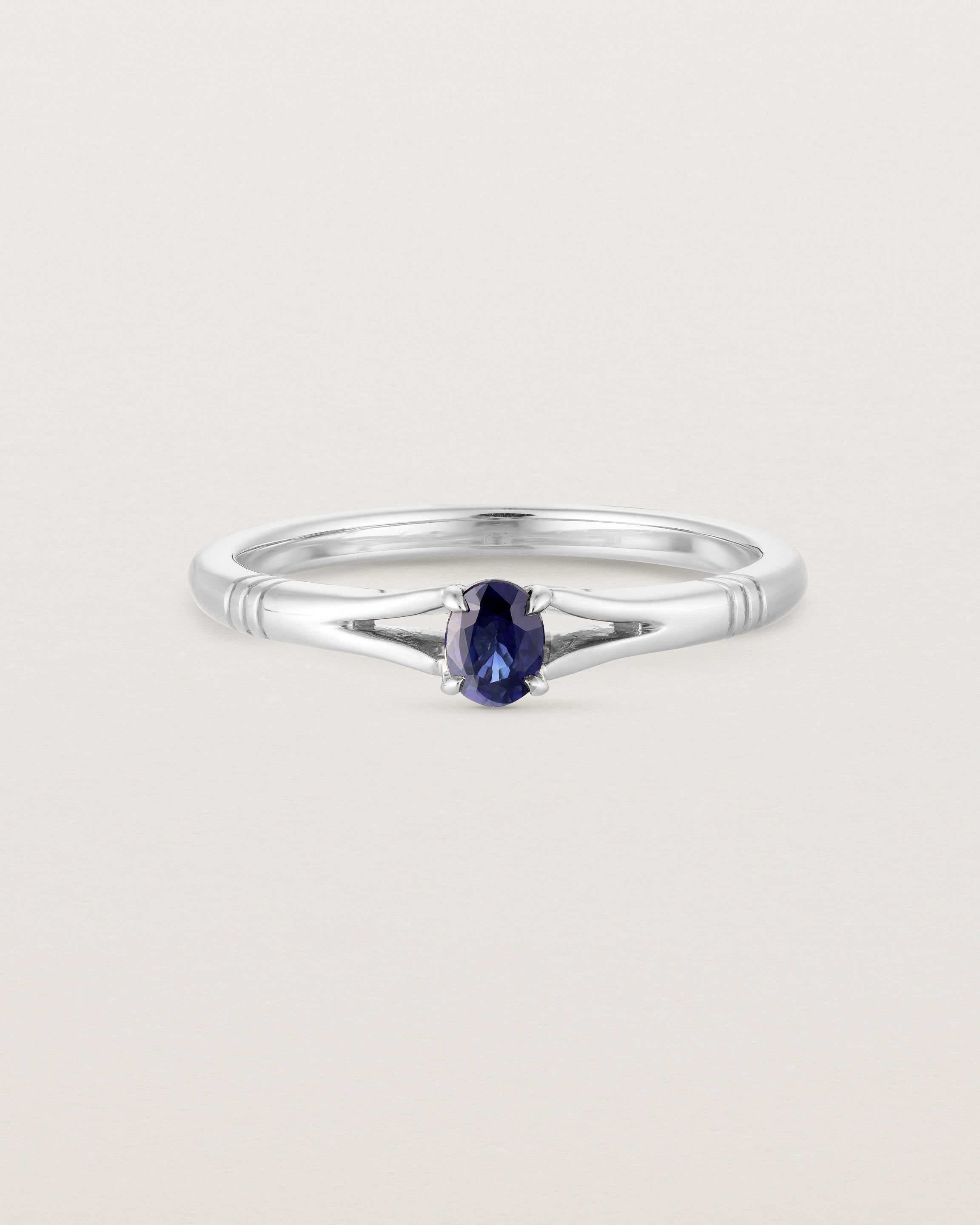 Front on deep etched image of a white gold engagement ring with an oval sapphire stone