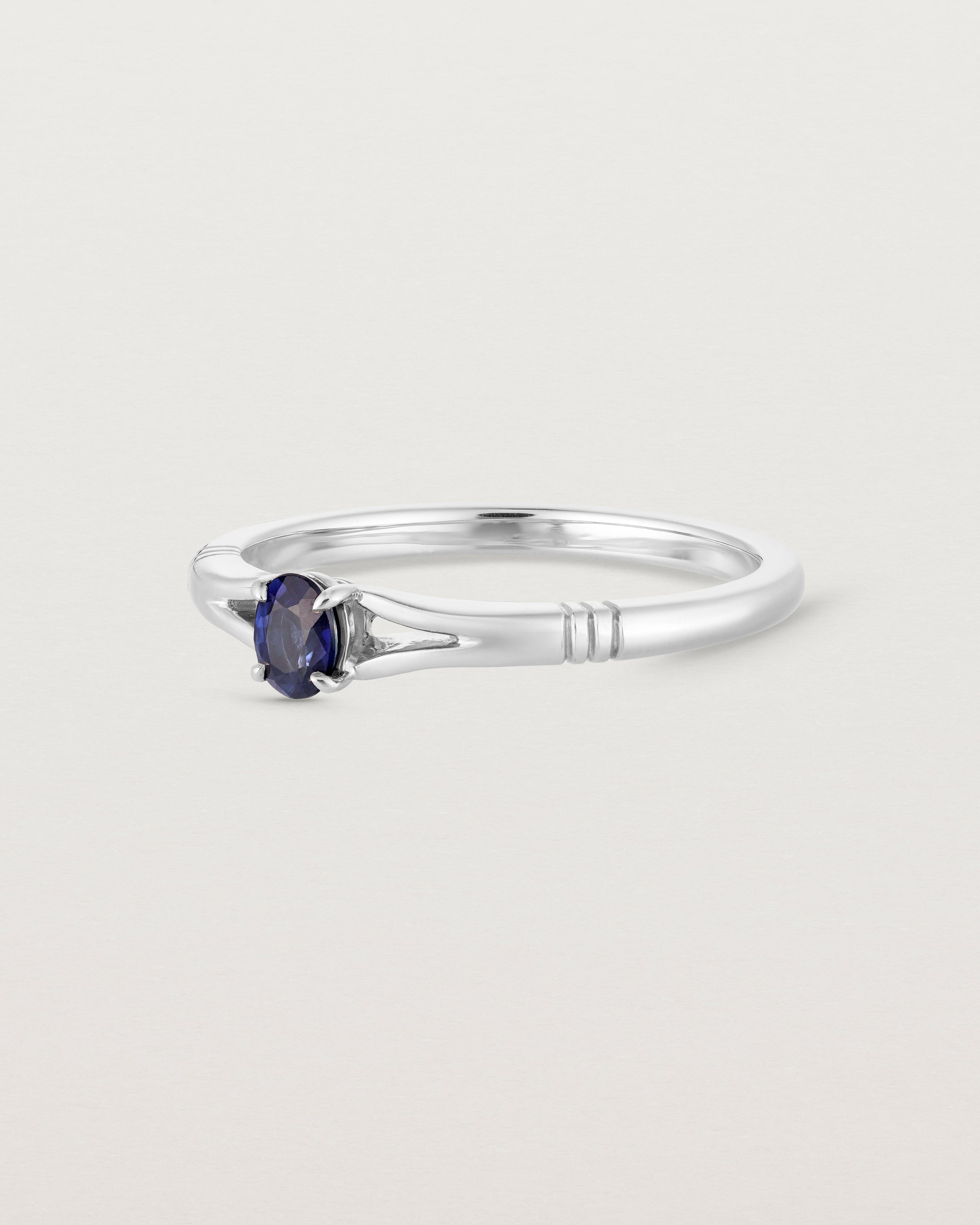 Side on deep etched image of a white gold engagement ring with an oval sapphire stone