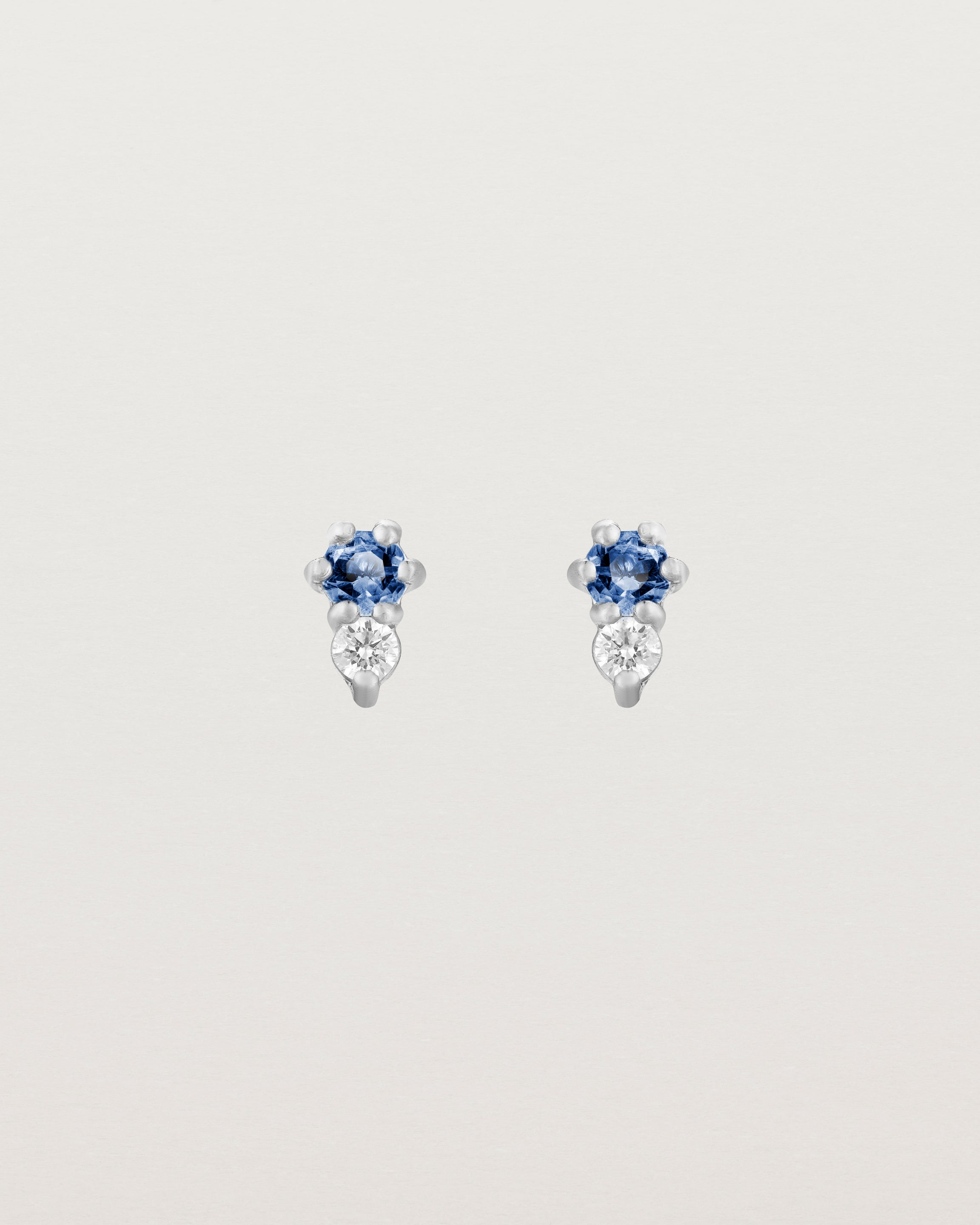 Front facing deep etched image of a pair of white gold earrings with blue sapphire birthstones and diamonds.