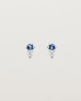 Front facing deep etched image of a pair of white gold earrings with blue sapphire birthstones and diamonds.