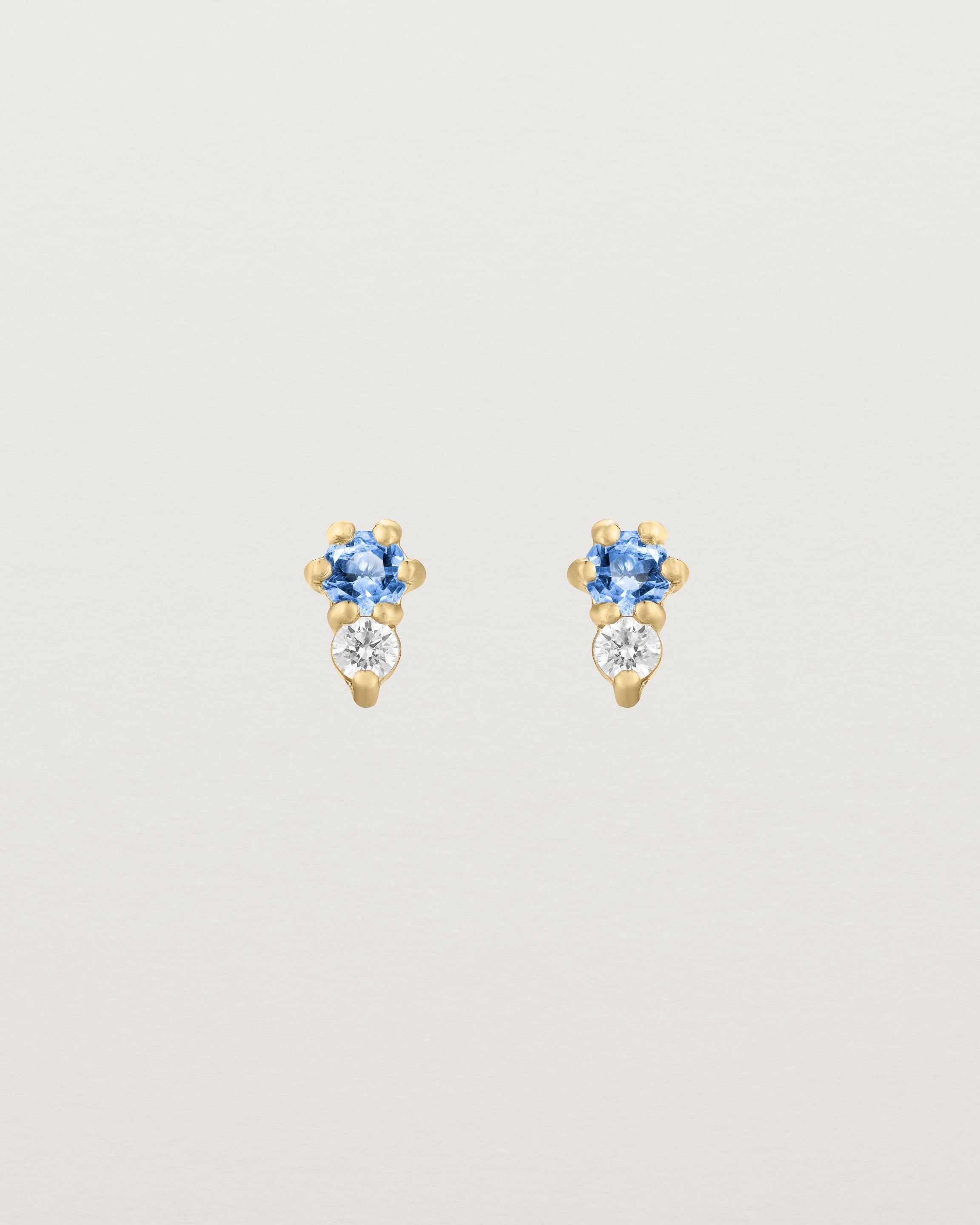 Front facing deep etched image of a pair of yellow gold earrings with blue topaz birthstones and diamonds.