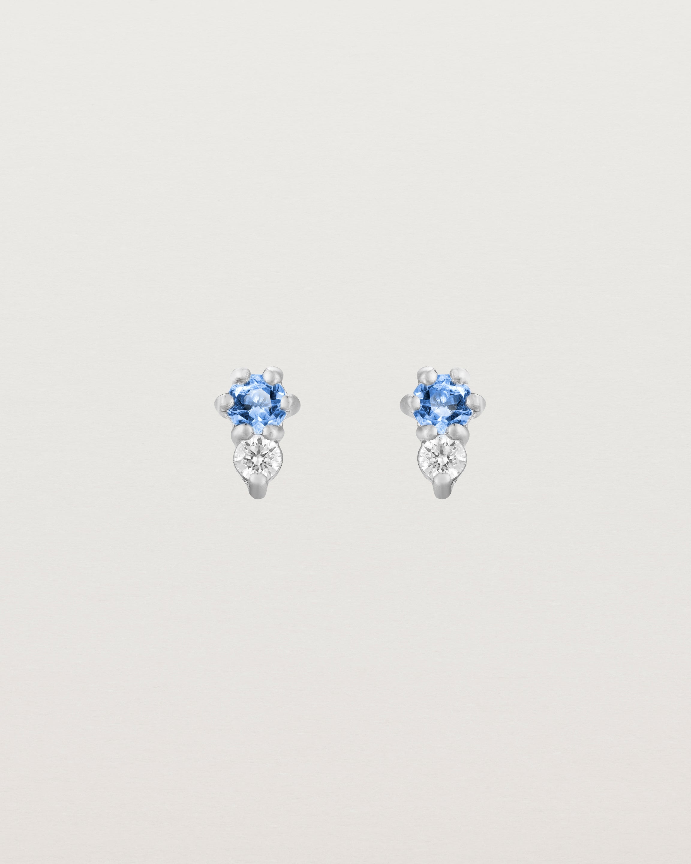 Front facing deep etched image of a pair of white gold earrings with blue topaz birthstones and diamonds.