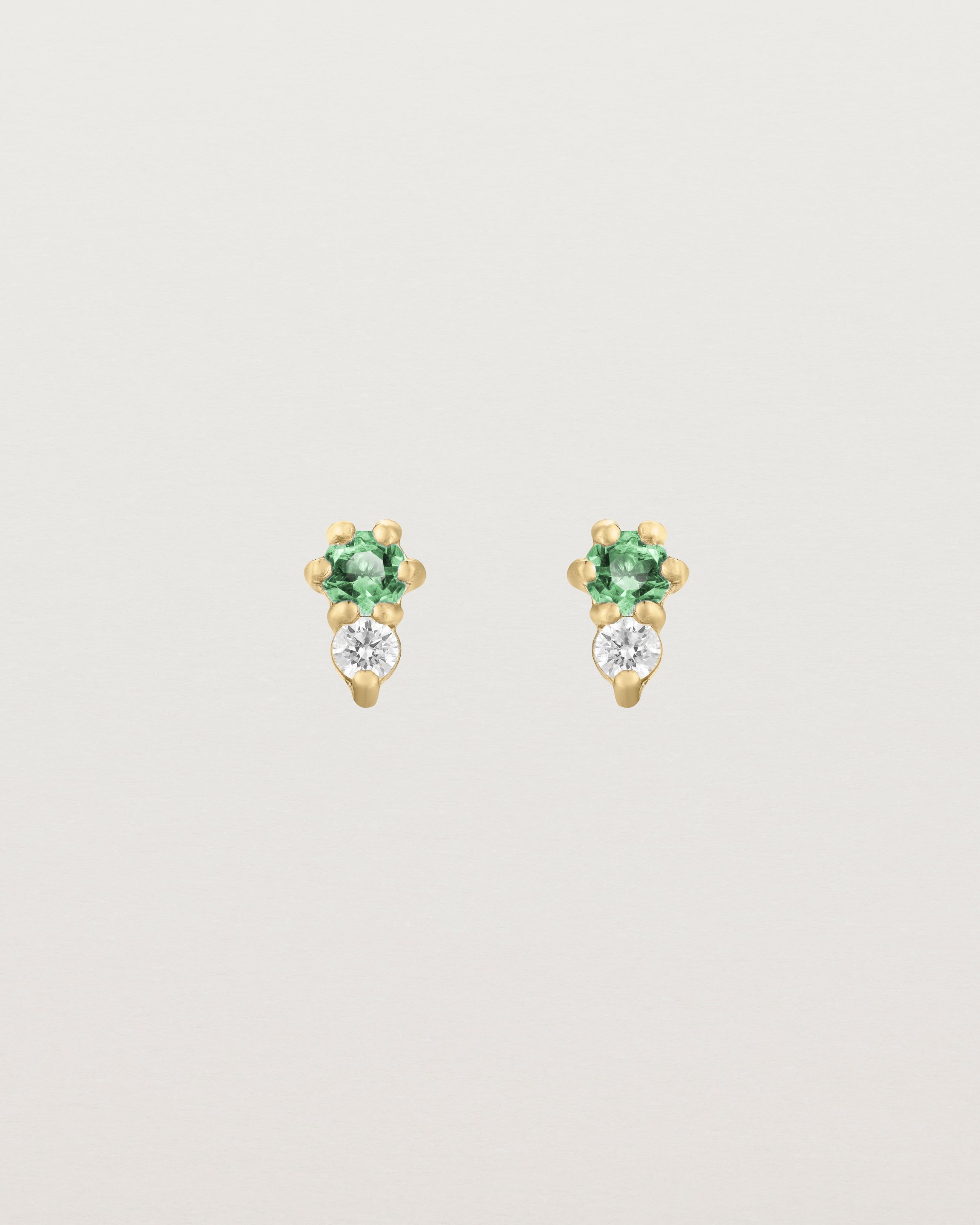 Front facing deep etched image of a pair of yellow gold earrings with emerald birthstones and diamonds.