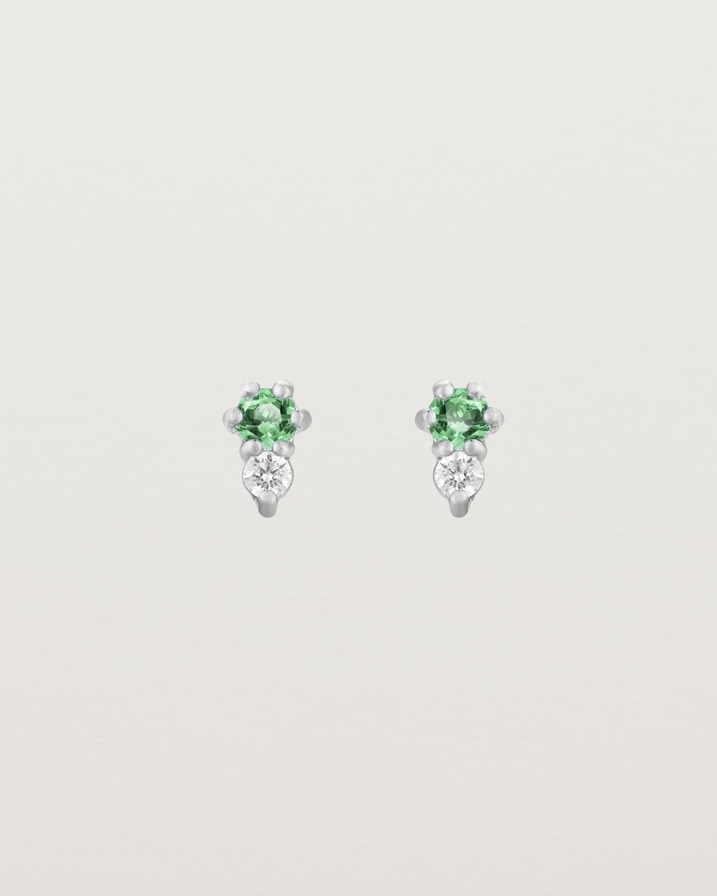 Front facing deep etched image of a pair of white gold earrings with emerald birthstones and diamonds.