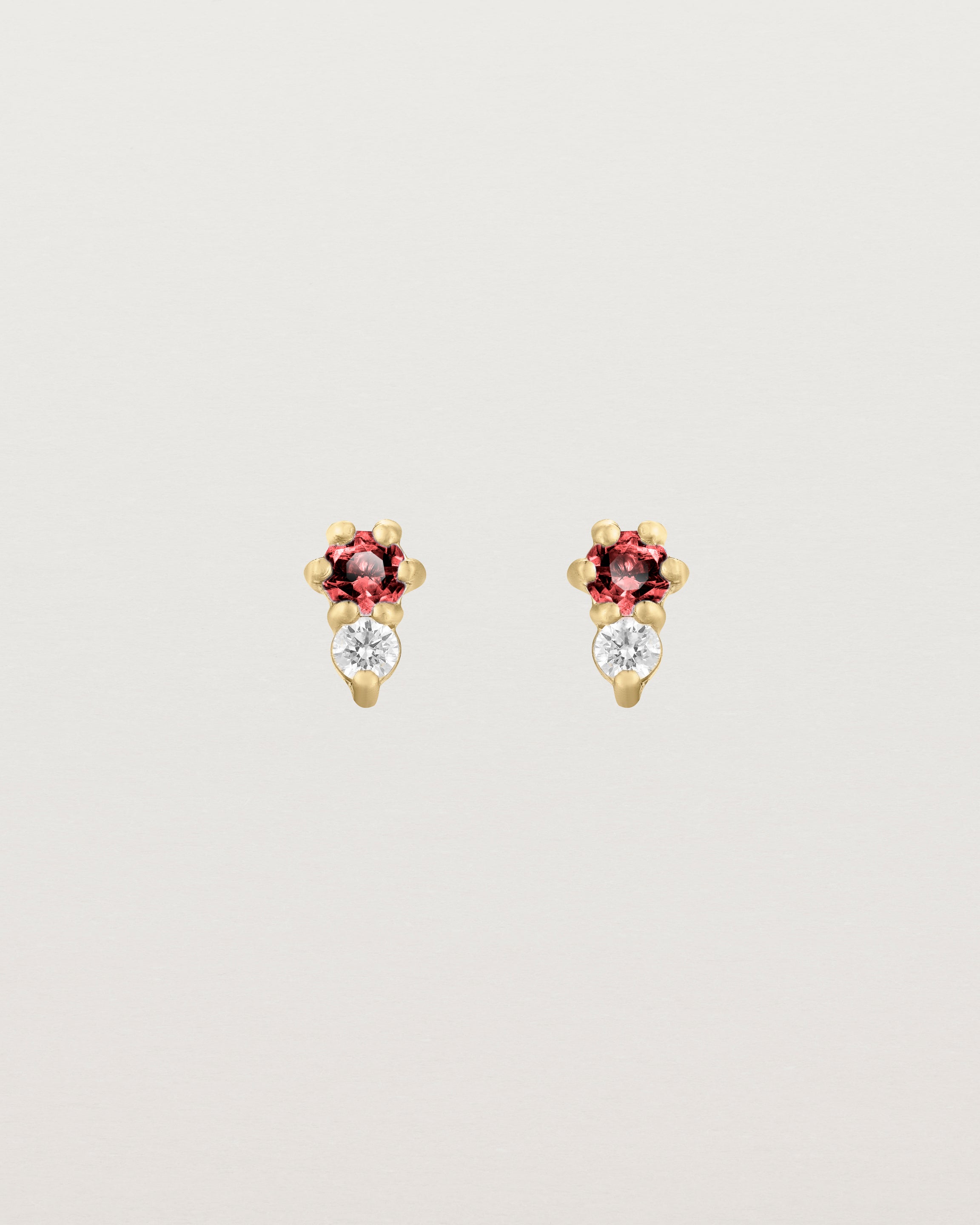 Front facing deep etched image of a pair of yellow gold earrings with ruby birthstones and diamonds.